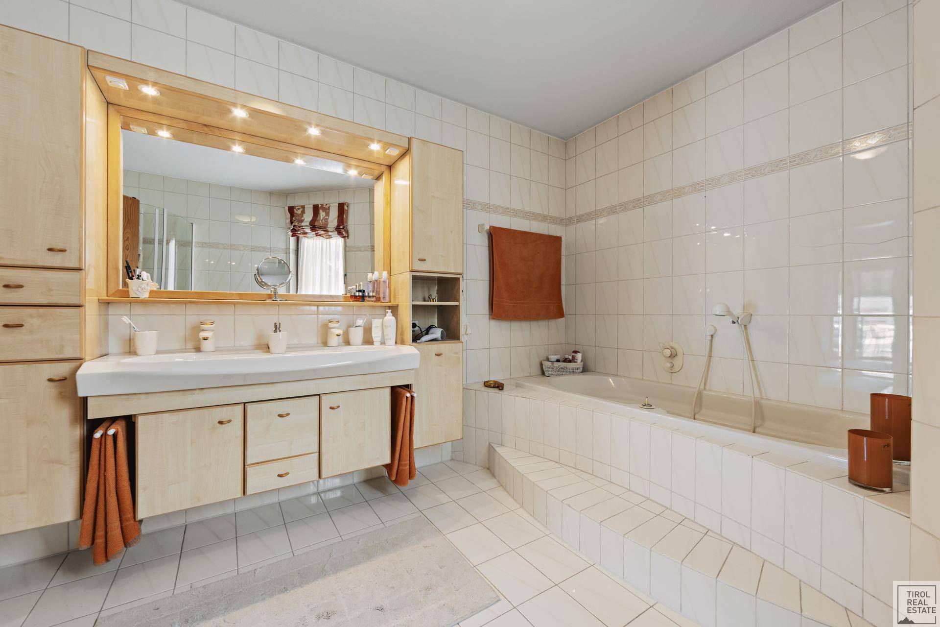 Geräumiges Badezimmer mit weißen Fliesen, Doppelwaschbecken und einer eingebauten Badewanne.