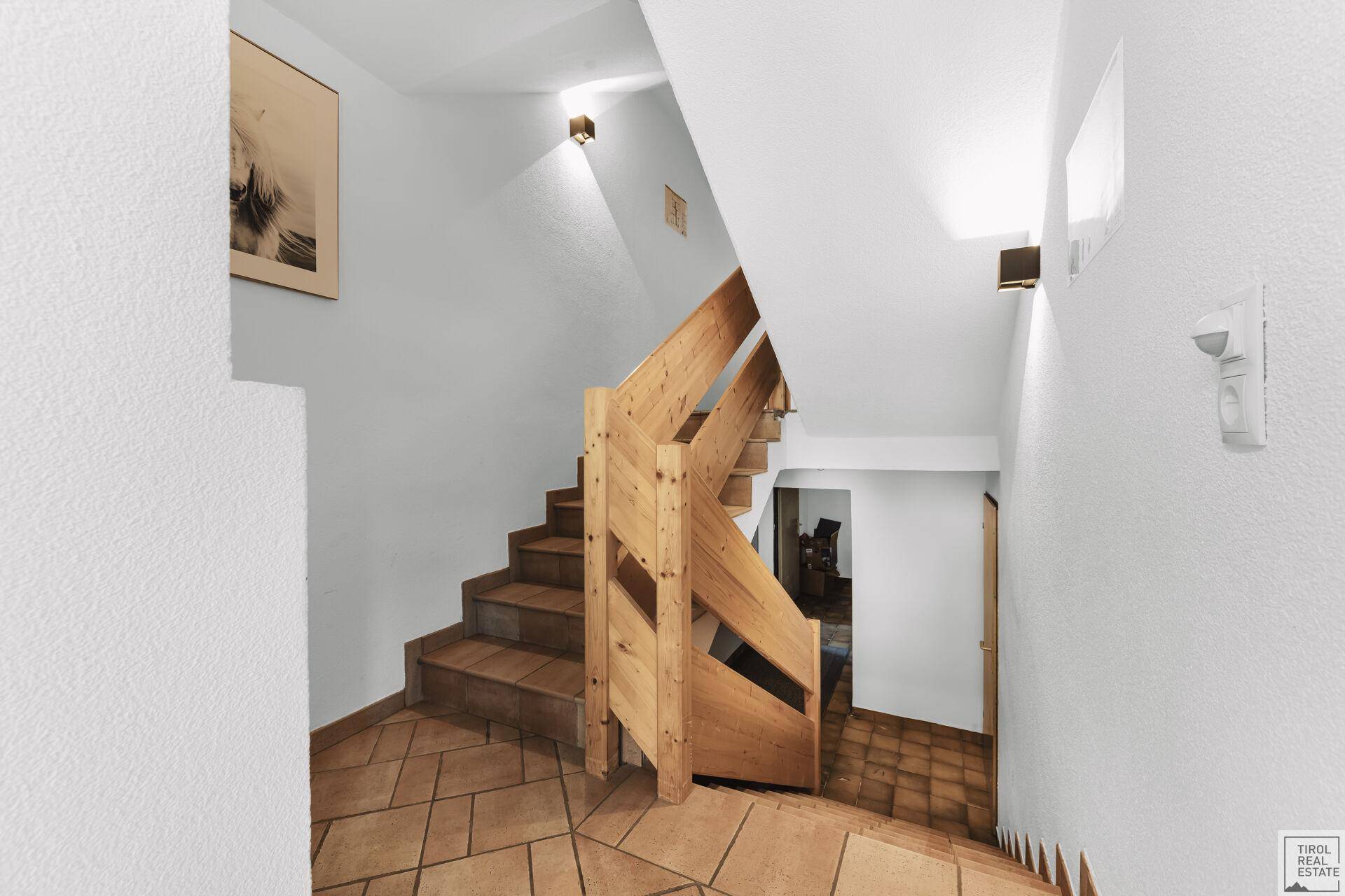 Heller Treppenaufgang mit Holzgeländer und Fliesenboden, der die Stockwerke verbindet.