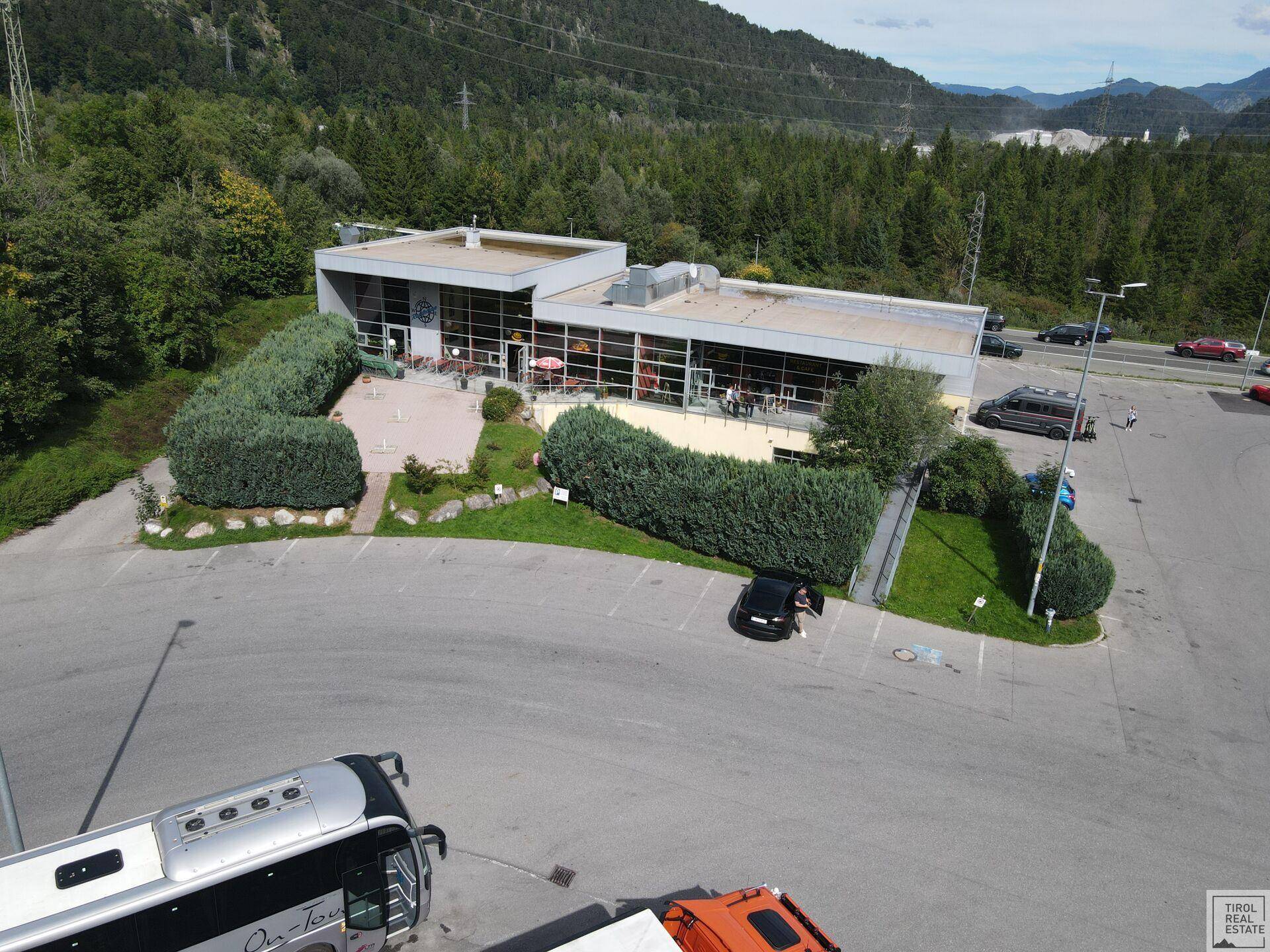 Übersicht des Gebäudes und des weitläufigen Parkplatzes, eingebettet in eine grüne Umgebung mit Bergen.
