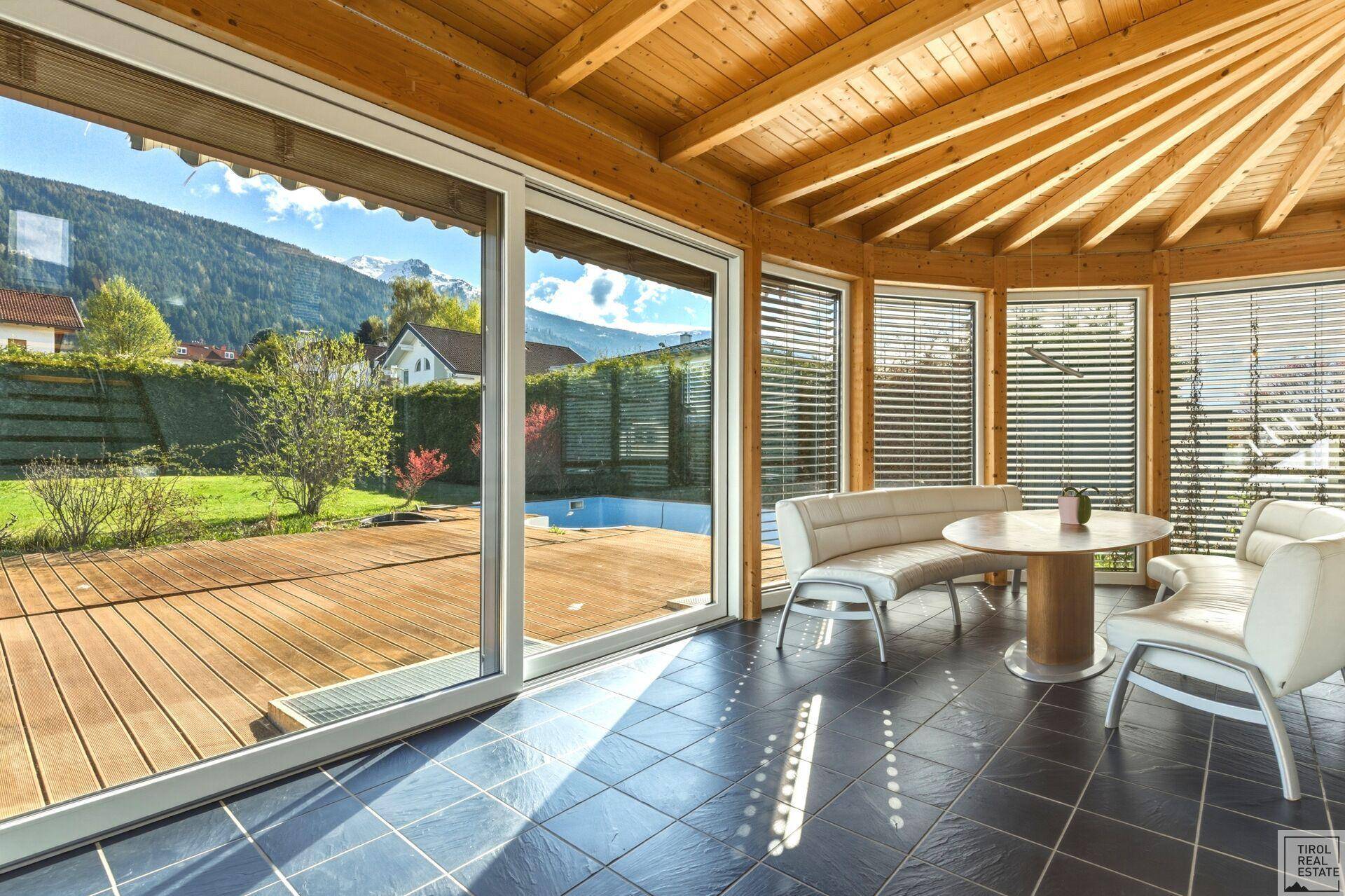 Heller Wintergarten mit Holzdach, großen Glasfronten und direktem Zugang zur Holzterrasse und Pool.