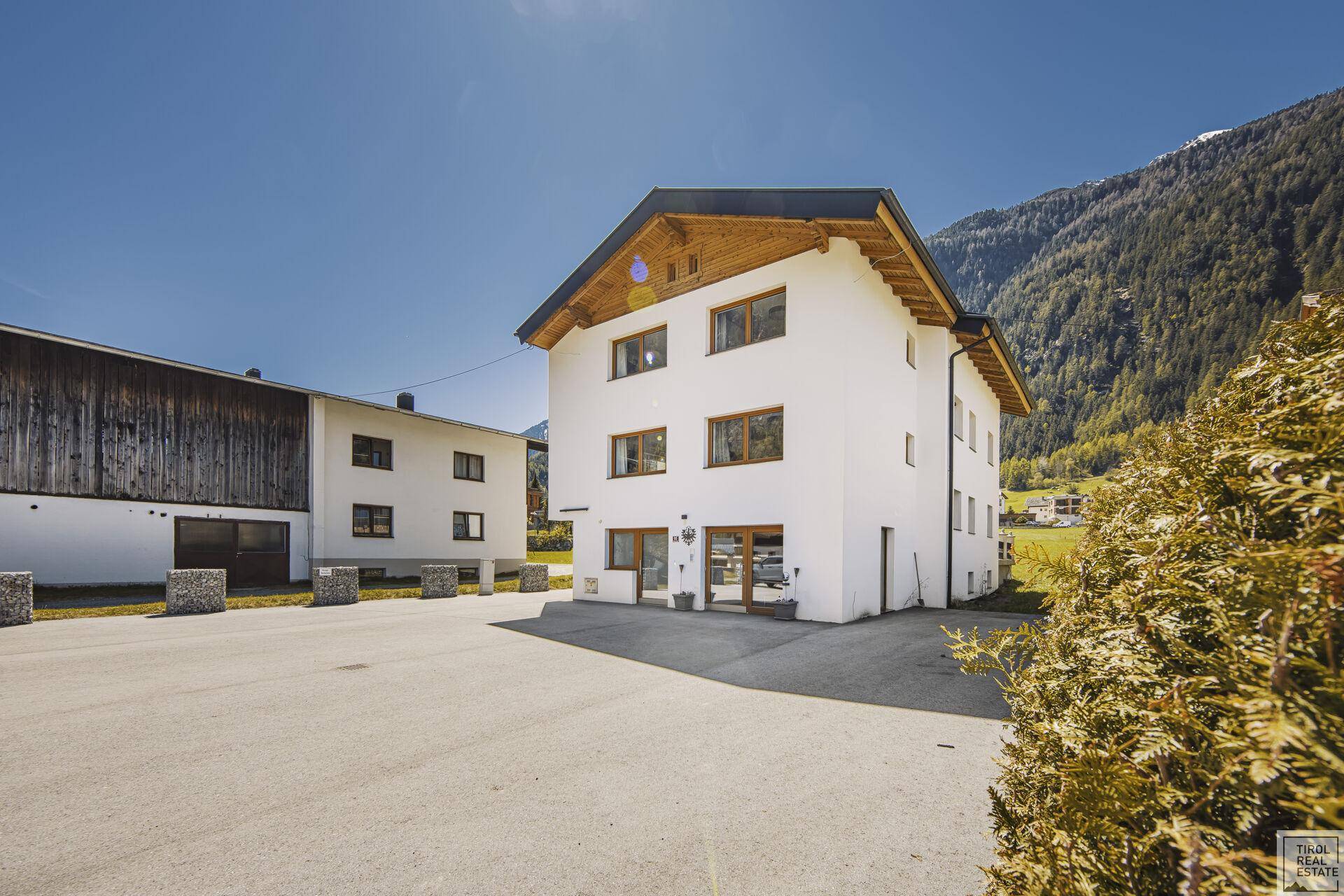 Seitenansicht des modernen Wohnhauses mit großem Parkplatz und traditionellem Holzdach.