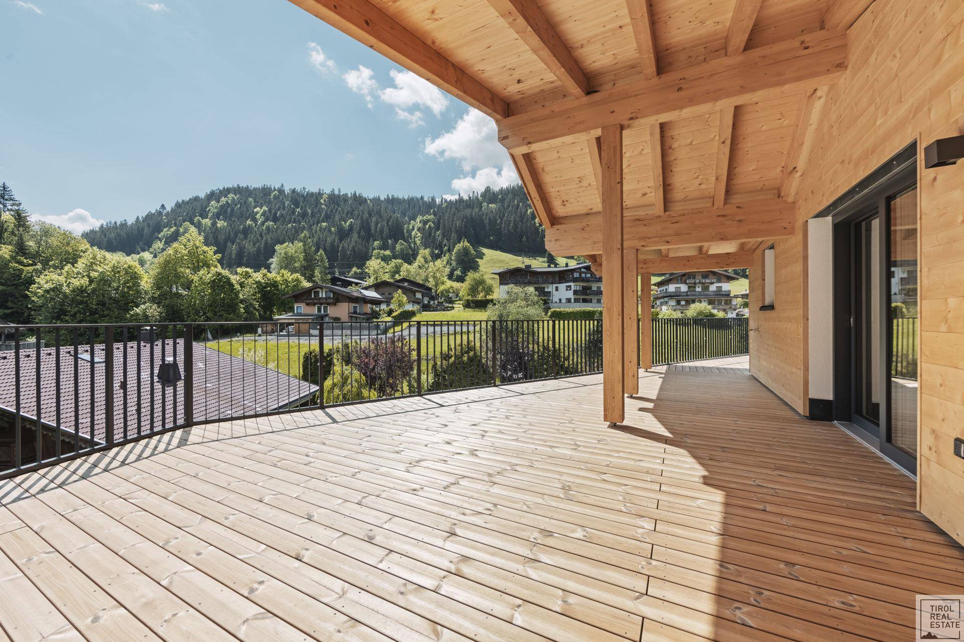Sonniger Terrassenbereich mit Holzboden und weitem Blick über die grüne Umgebung und Häuser.