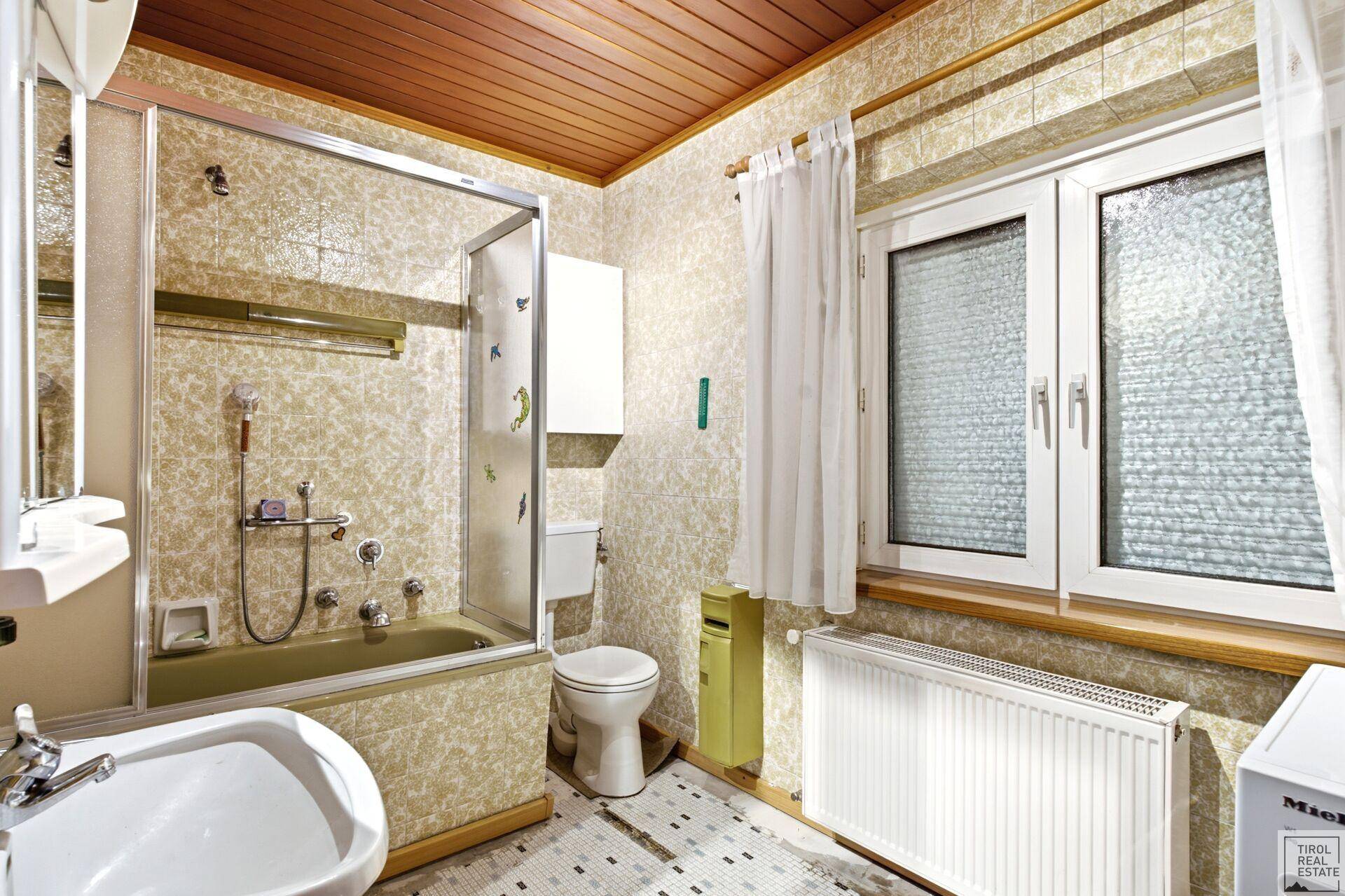 Badezimmer im Stil der 80er Jahre mit grüner Badewanne, Bidet und Fenster.