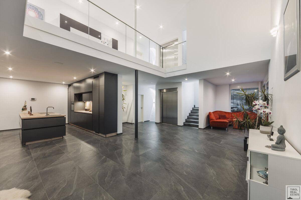 Modernes, offenes Wohnzimmer mit integrierter Küche, Galerie und dunklen Fliesenboden.