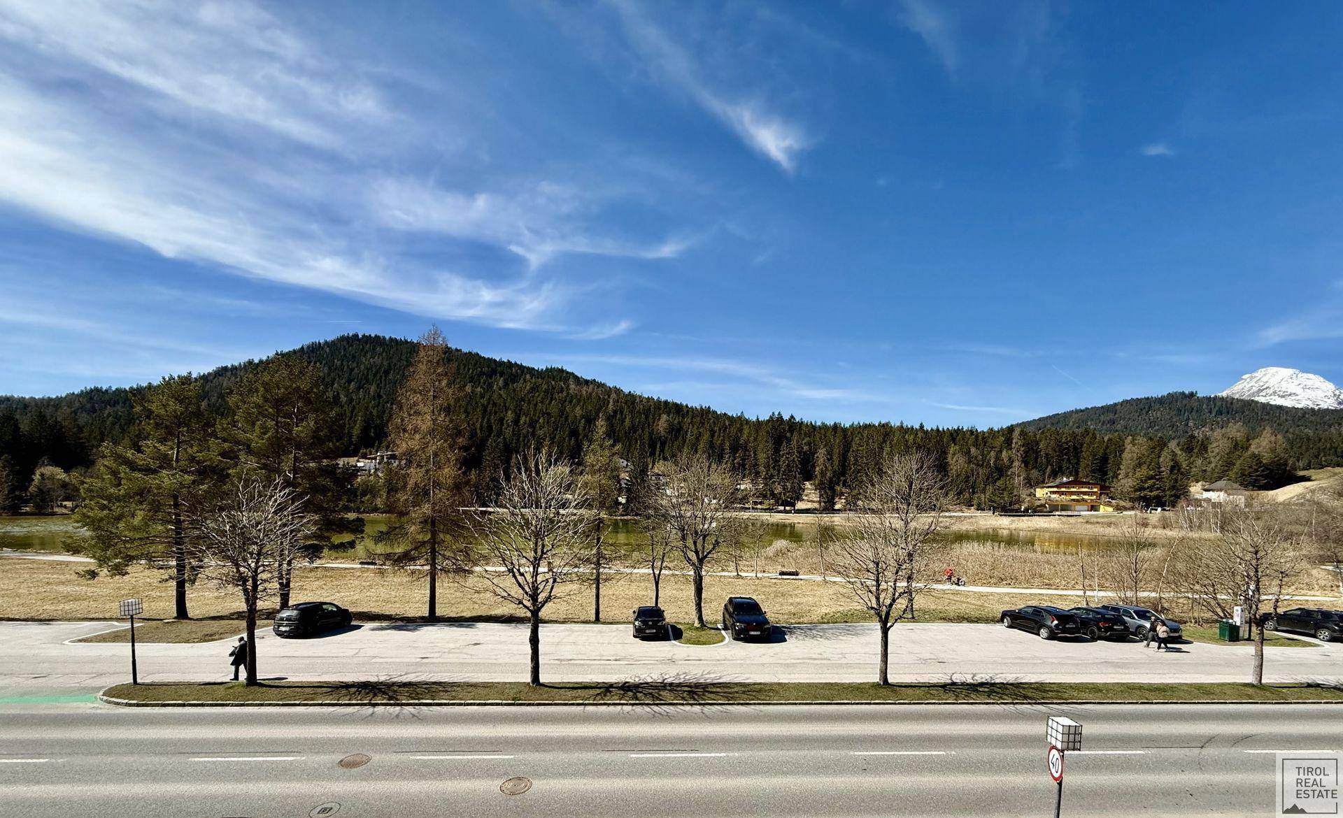 Panoramablick auf die Umgebung mit Straße, Parkplätzen und bewaldeten Hügeln.