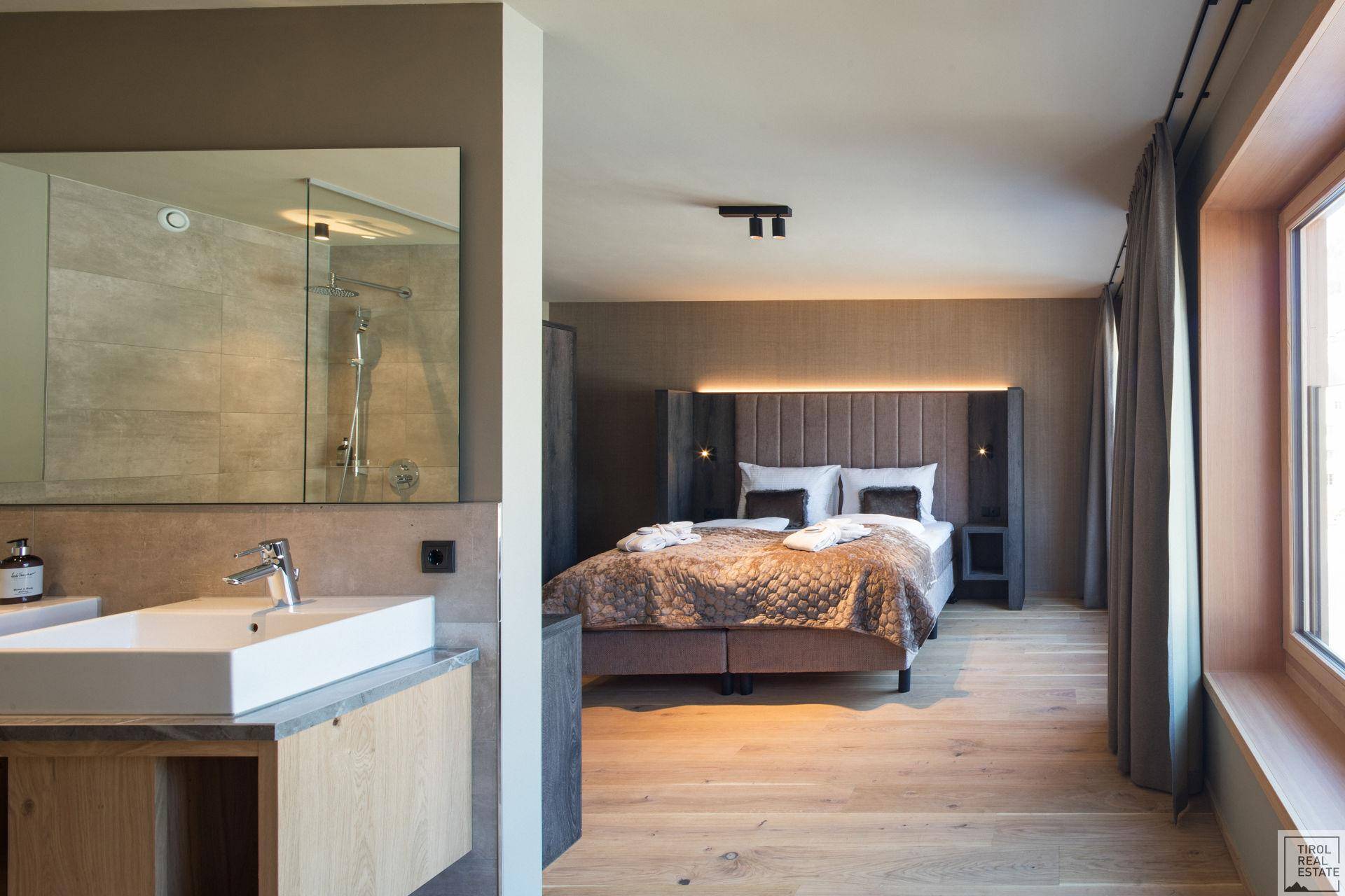 Modernes Schlafzimmer mit offenem Badbereich, Doppelbett und Holzboden, stilvoll und funktional.