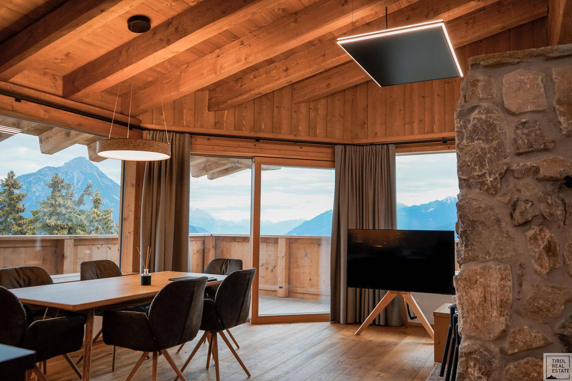 Geräumiger Wohn-Essbereich mit rustikalen Holzelementen, Steinkamin und weitem Bergblick.
