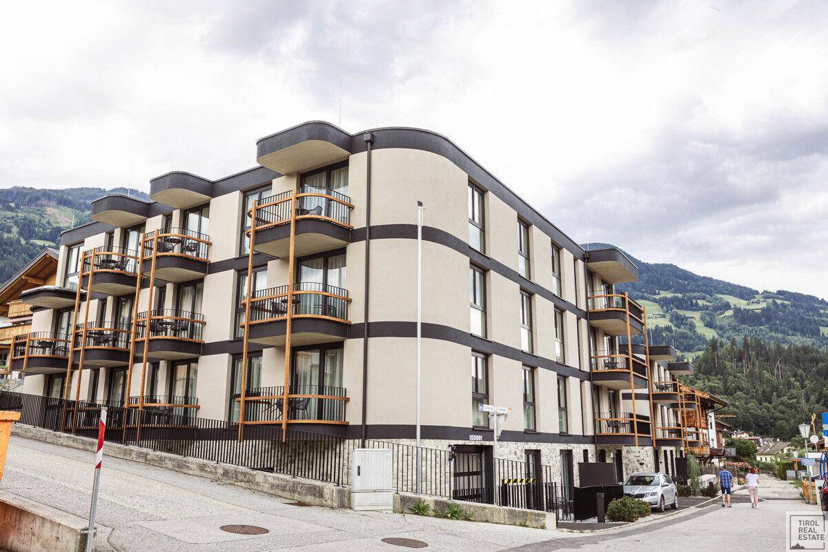Modernes Apartmentgebäude mit geschwungenen Balkonen und Blick auf die umliegende Berglandschaft.