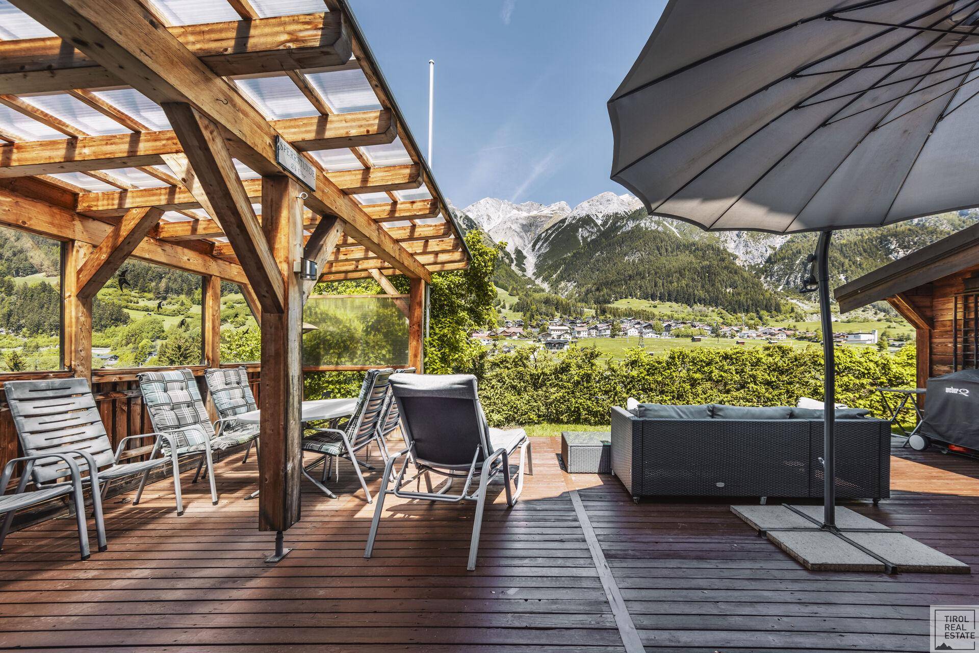 Geräumige Holzterrasse mit Pergola, Essbereich und Lounge-Möbeln mit Bergblick.