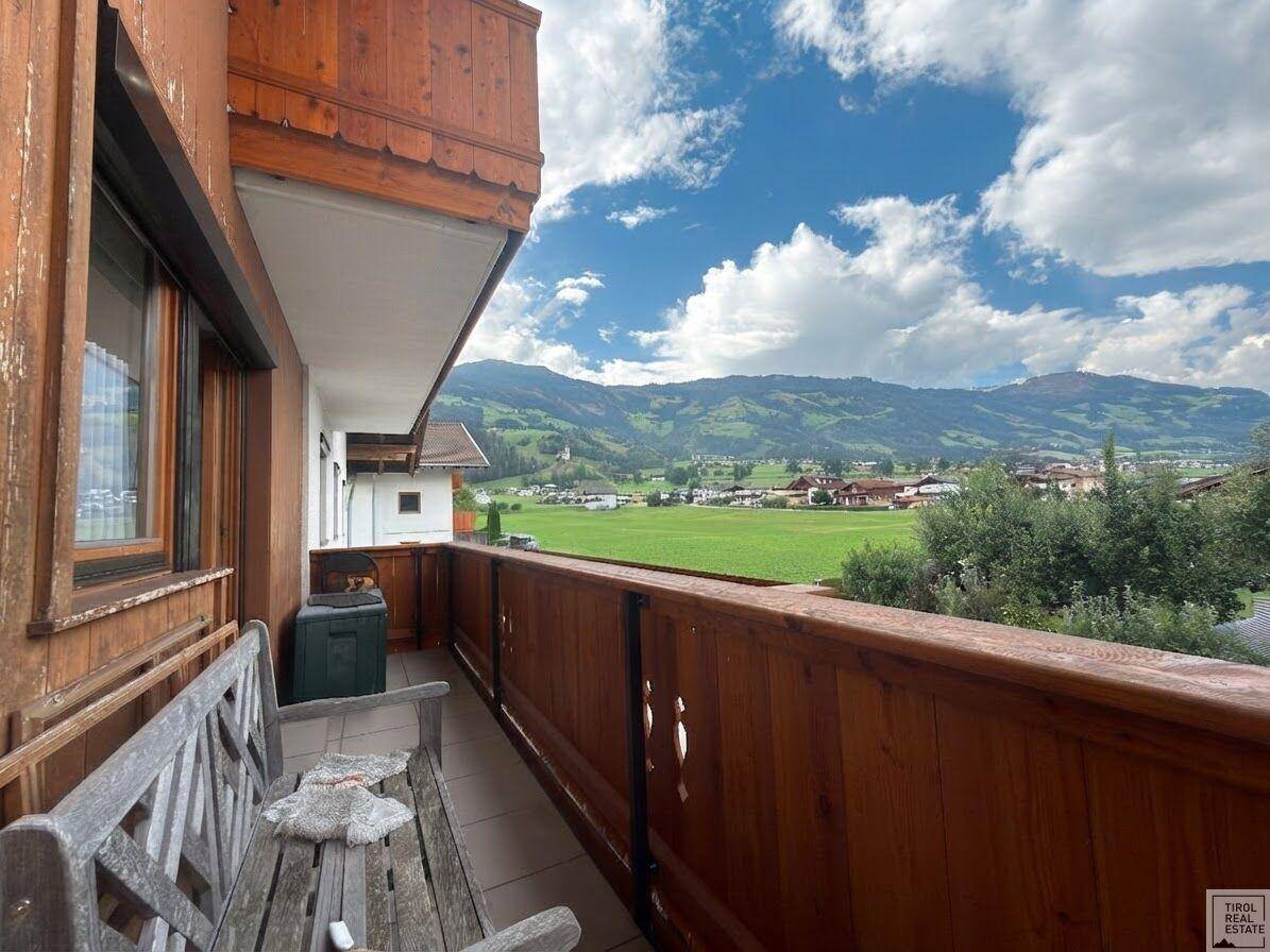 Geräumiger Balkon mit Holzbank und weitem Blick über die Landschaft und Berge.