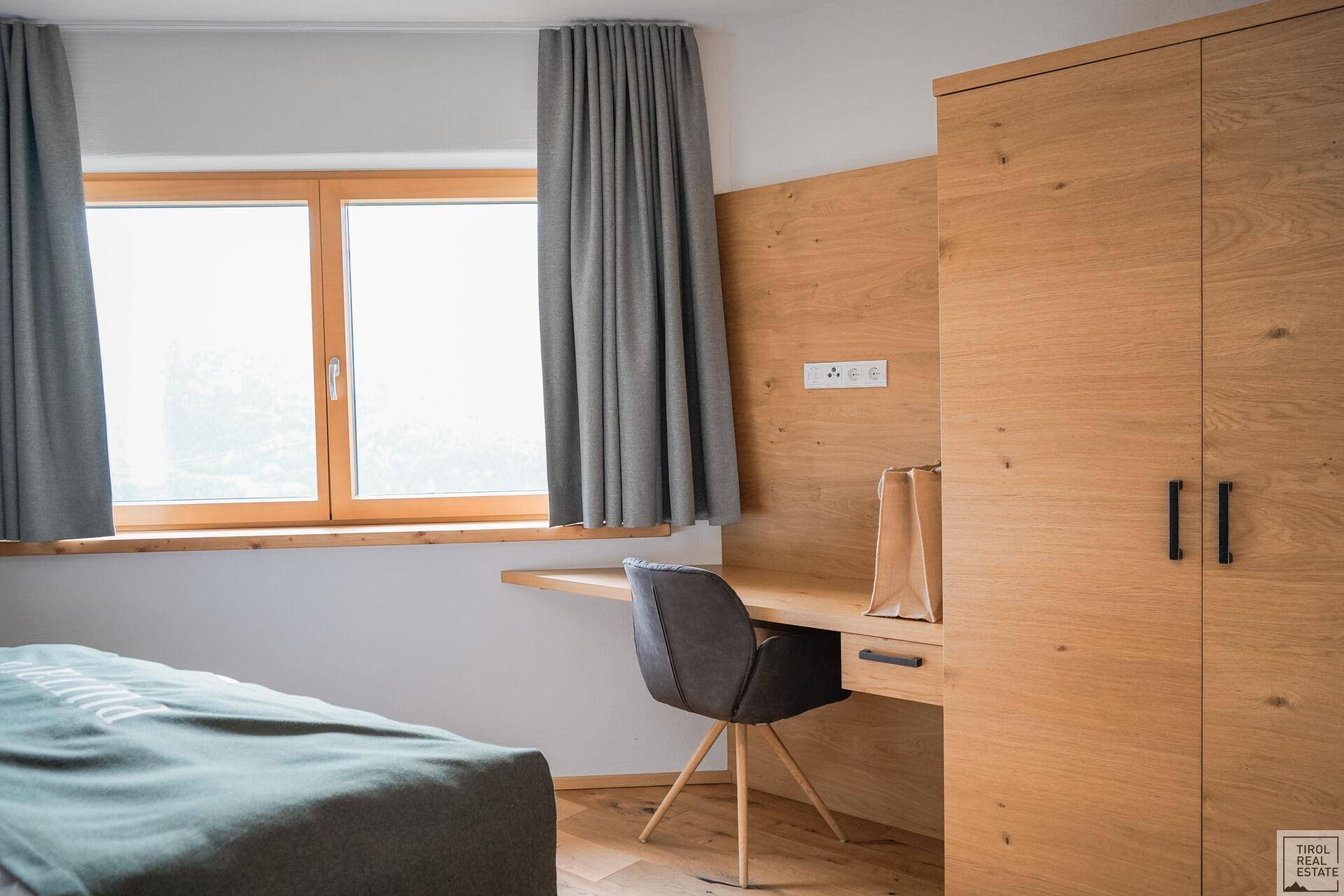 Schlafzimmer mit integriertem Schreibtischbereich, Holzboden und großem Fenster.