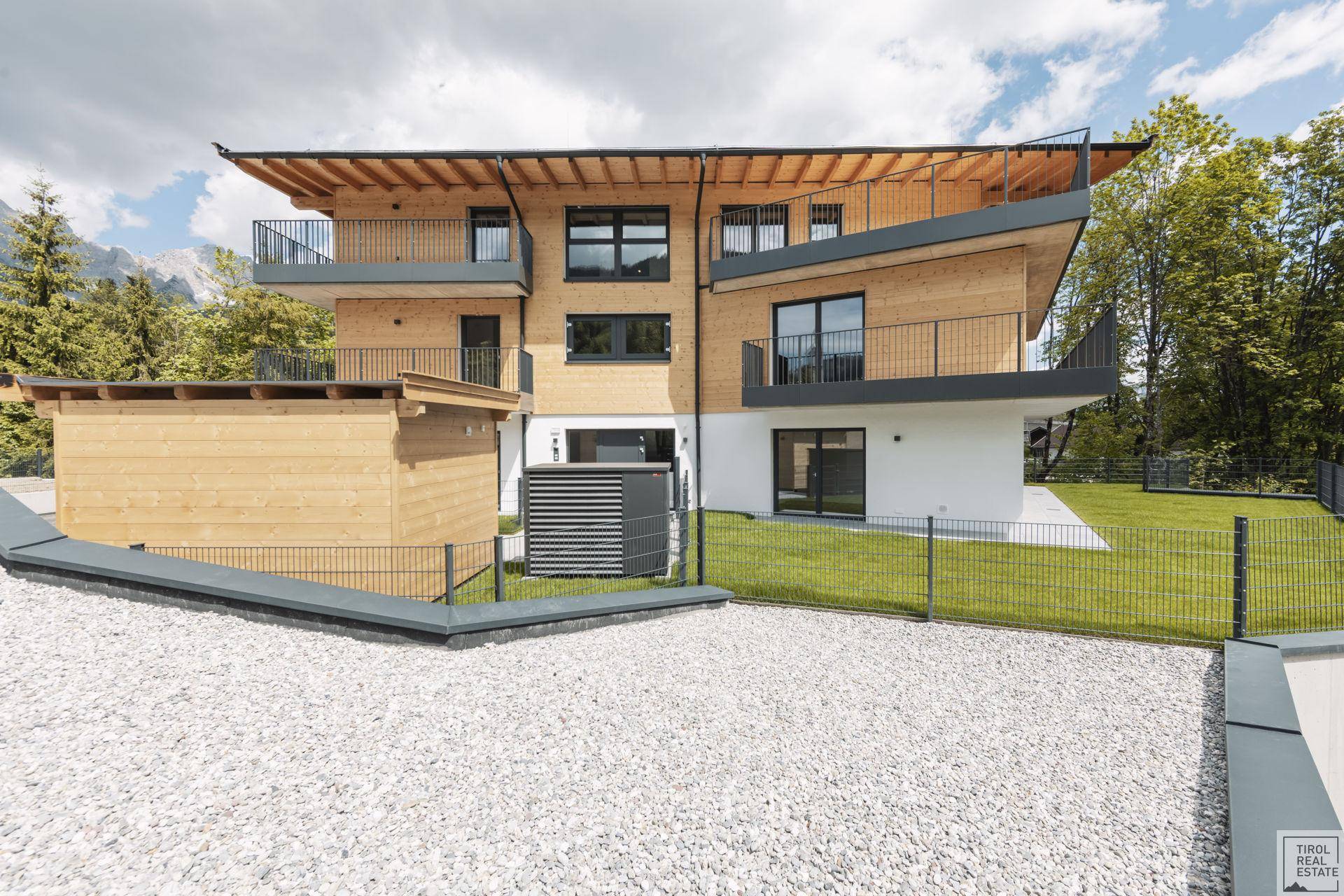 Modernes Holzhaus mit Balkonen und gepflegtem Vorgarten, umgeben von Natur.