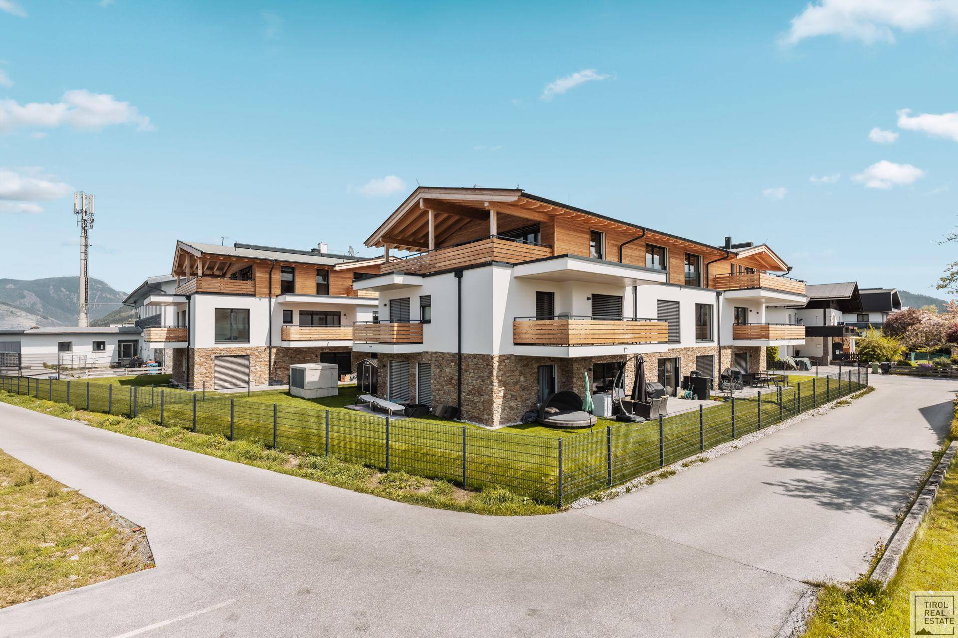 Moderne Wohnanlage mit mehreren Balkonen und Gärten in einer grünen Umgebung.