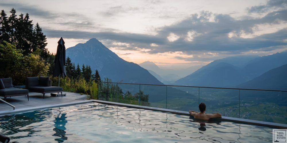 Person entspannt im Infinity-Pool mit atemberaubendem Panoramablick auf die Berge bei Sonnenuntergang.