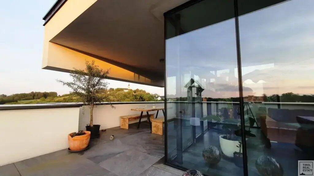 Geräumige Terrasse mit Fliesenboden und einem kleinen Baum, bietet weite Aussicht auf die Landschaft.