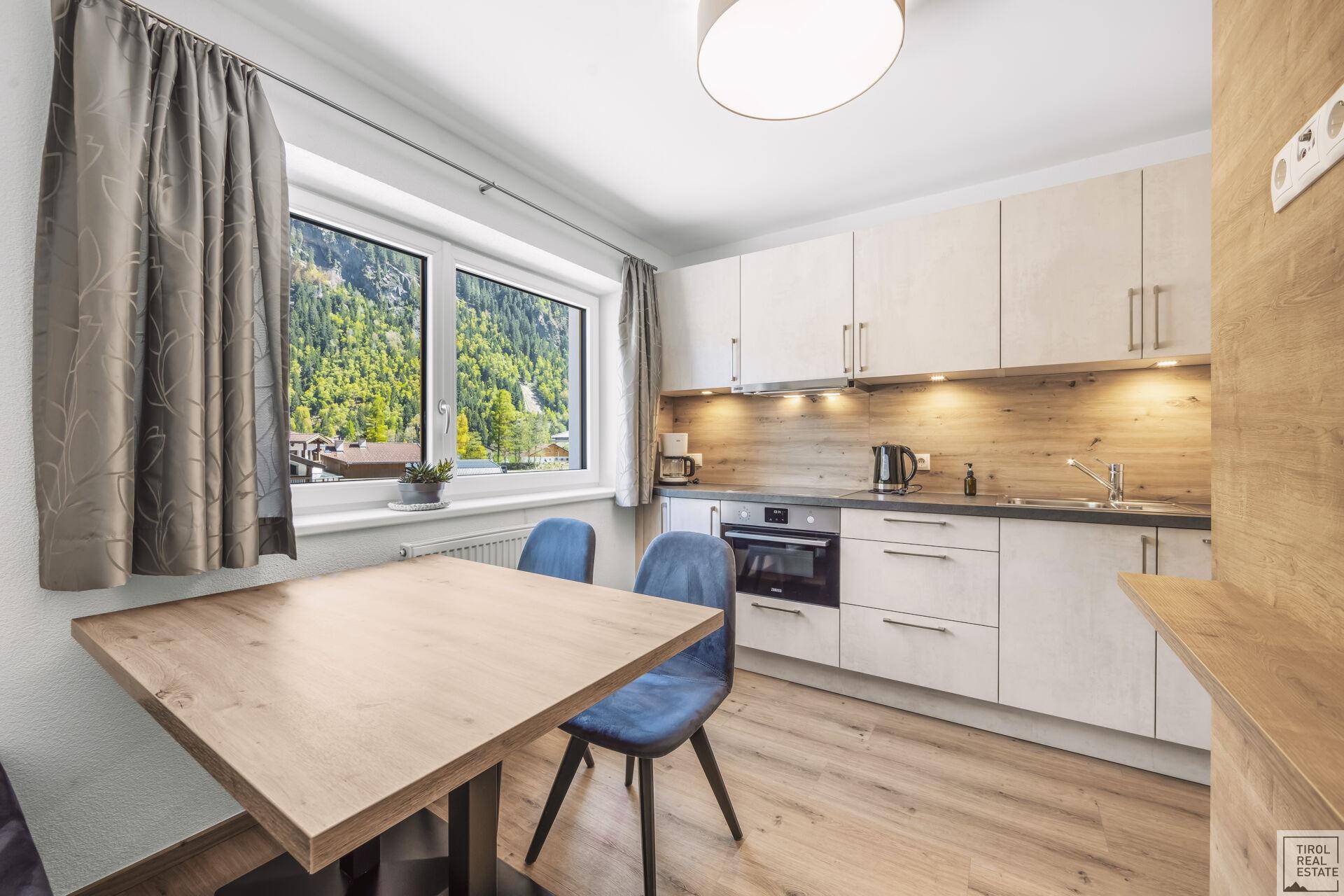 Helle Küche mit Essbereich, modernen Geräten und Fenster mit Blick auf die Berge.