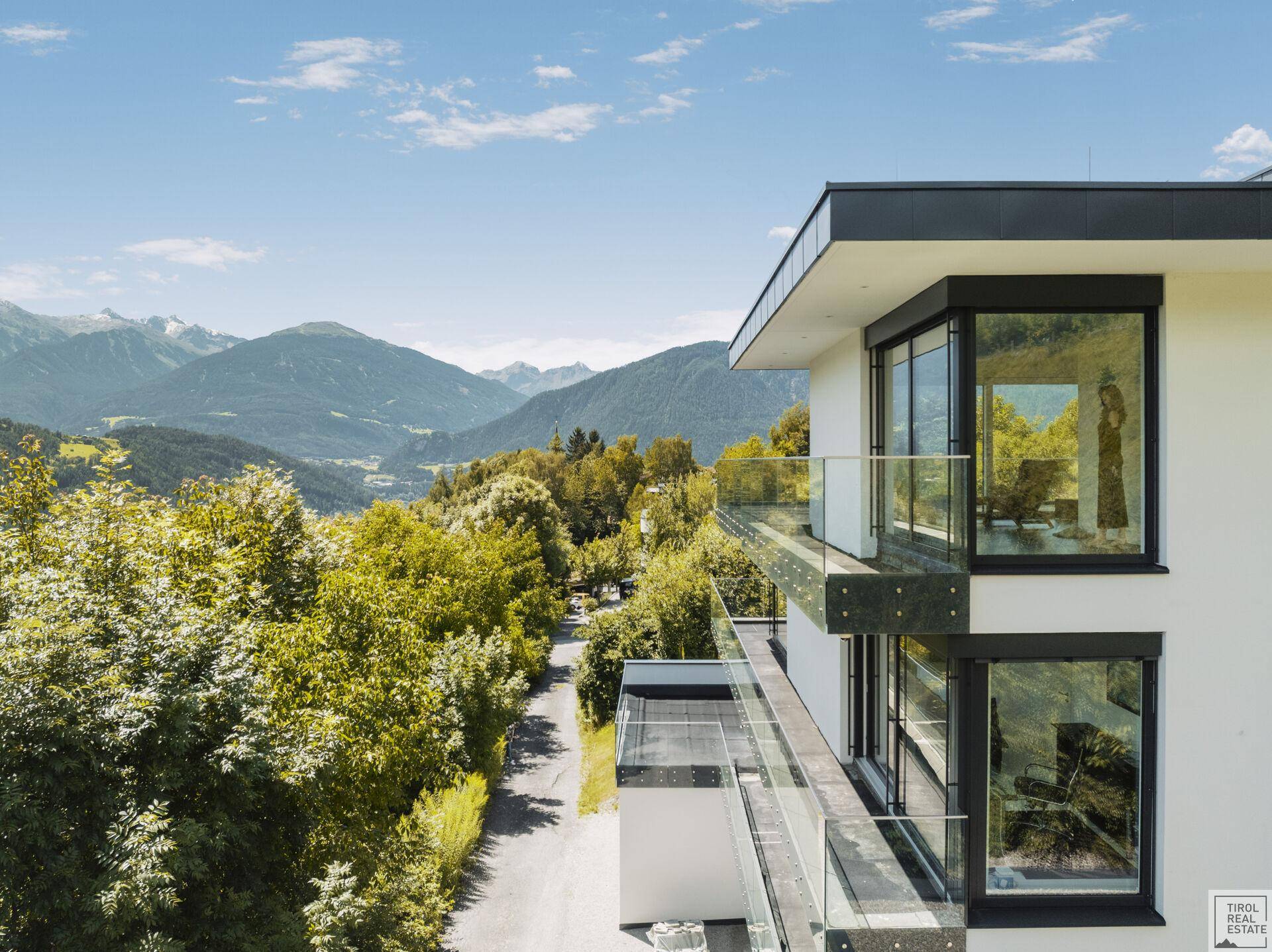 Moderne Architektur mit Glasbalkonen und weitem Blick über die grüne Berglandschaft.