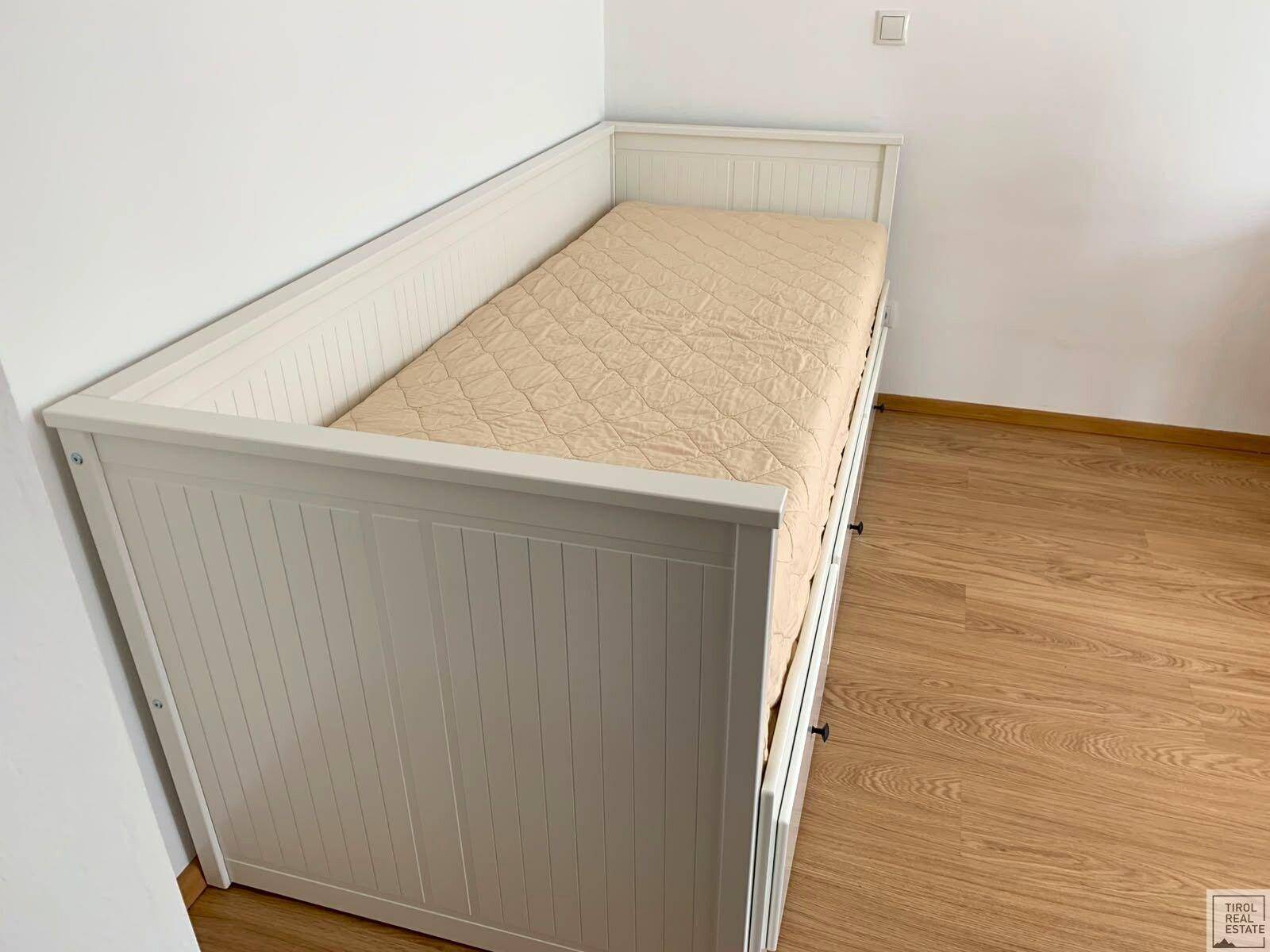 Detailansicht eines weißen Tagesbetts mit Stauraumschubladen und beiger Matratze auf Holzboden.