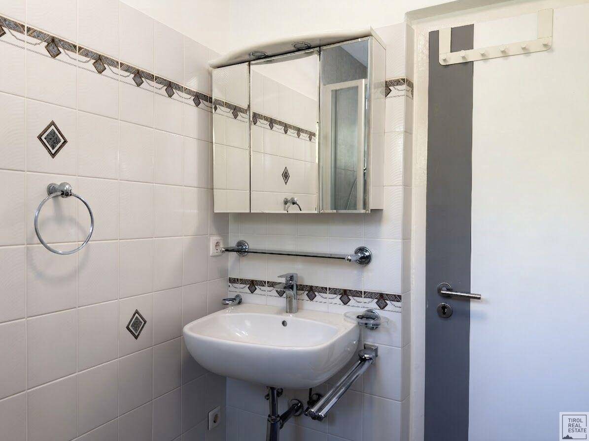 Badezimmer mit Waschbecken, Spiegelschrank und Fliesen in Weiß und Grau.
