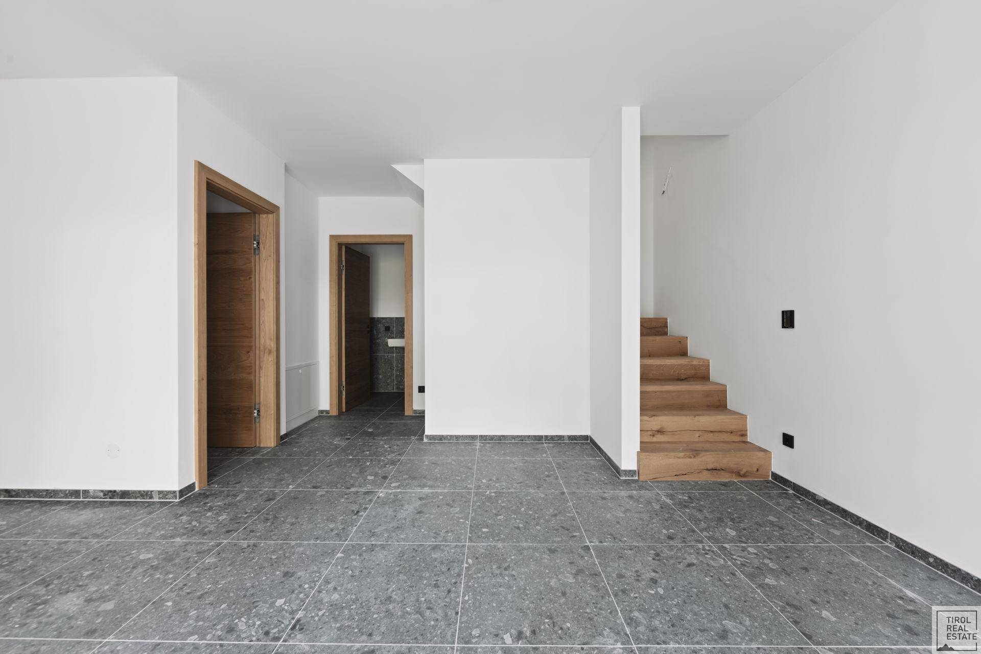 Eingangsbereich mit modernen grauen Fliesen und einer Holztreppe, die in die obere Etage führt.