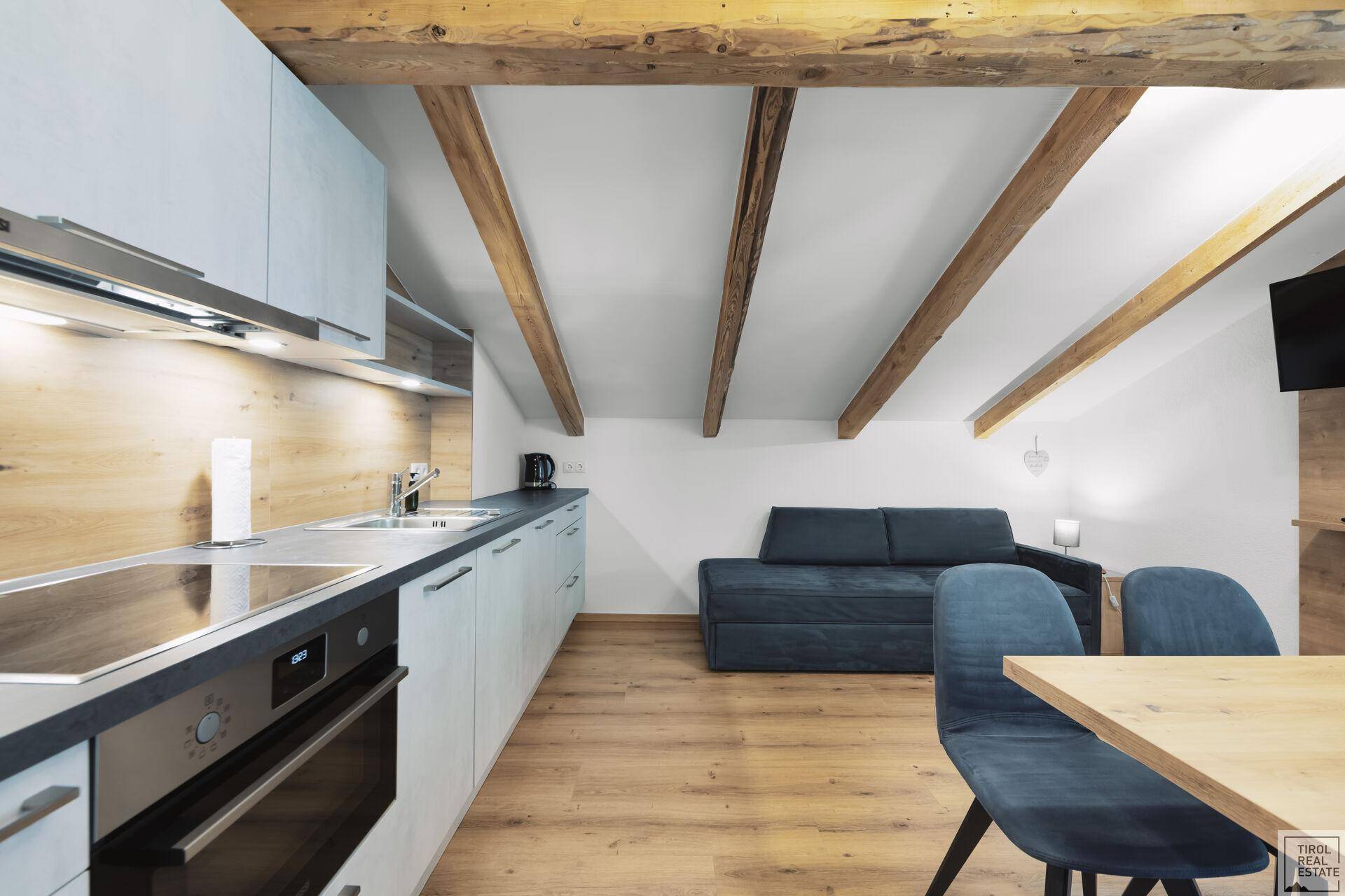 Moderne Küche mit Essbereich, Holzbalken und angrenzendem Wohnbereich unter dem Dach.