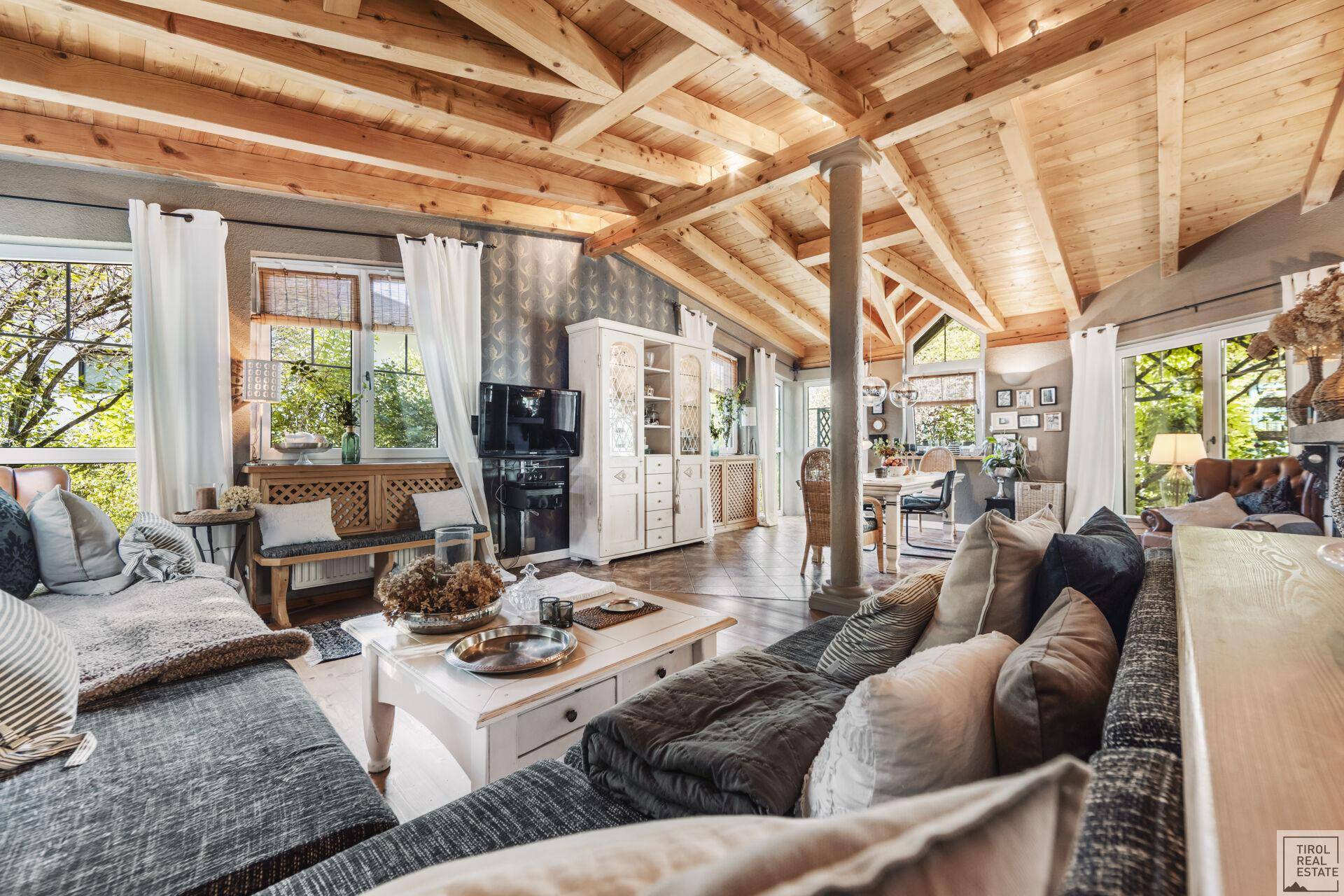 Heller Wohn- und Essbereich mit Holzbalkendecke, großem Sofa und Blick in den Garten.