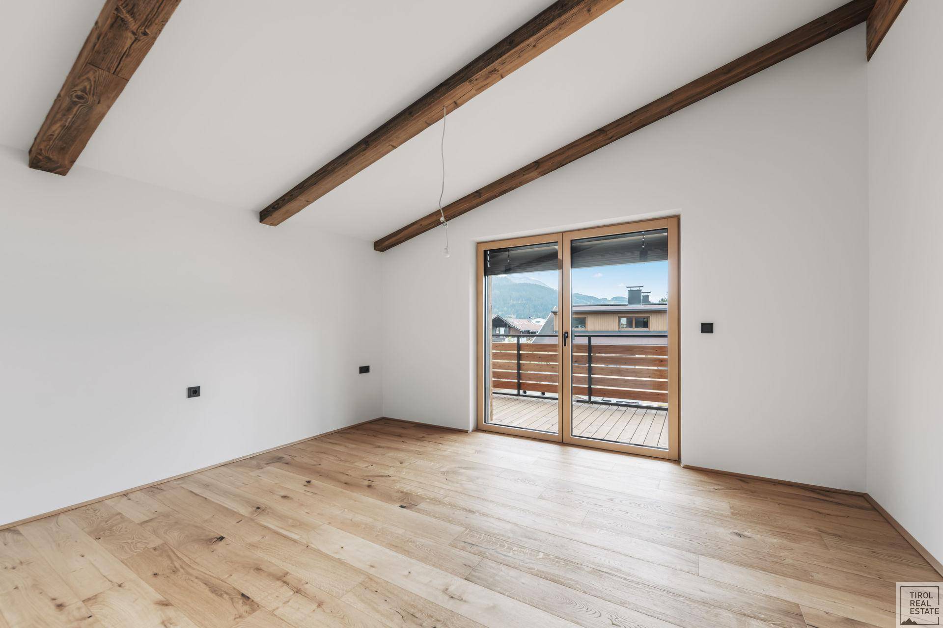 Geräumiges Zimmer mit Holzbalken, Parkettboden und großer Schiebetür zur Außenterrasse.