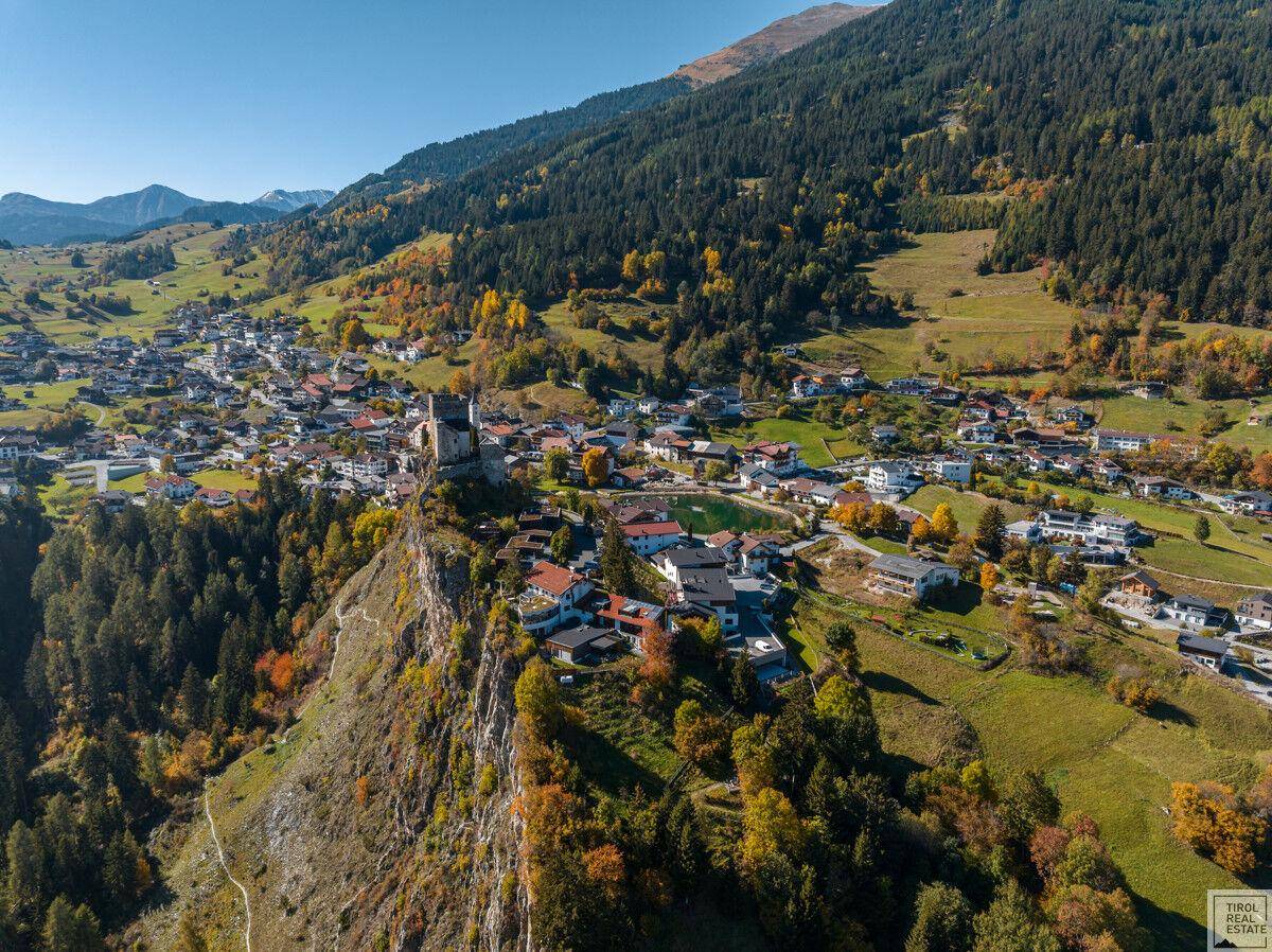 Malerische Luftaufnahme eines Bergdorfes mit historischer Burg und herbstlicher Vegetation.