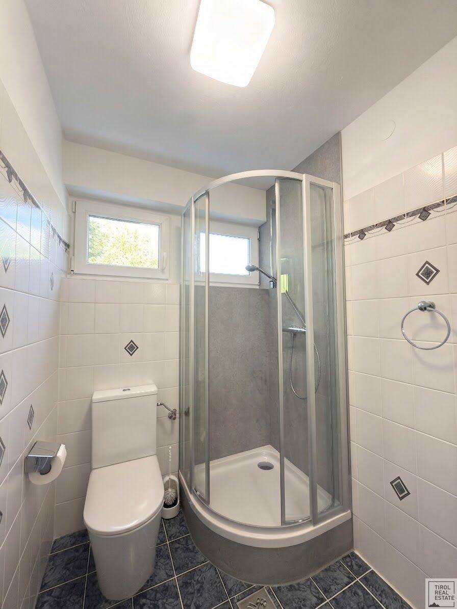 Badezimmer mit Duschkabine, WC und zwei Fenstern für natürliche Belüftung.