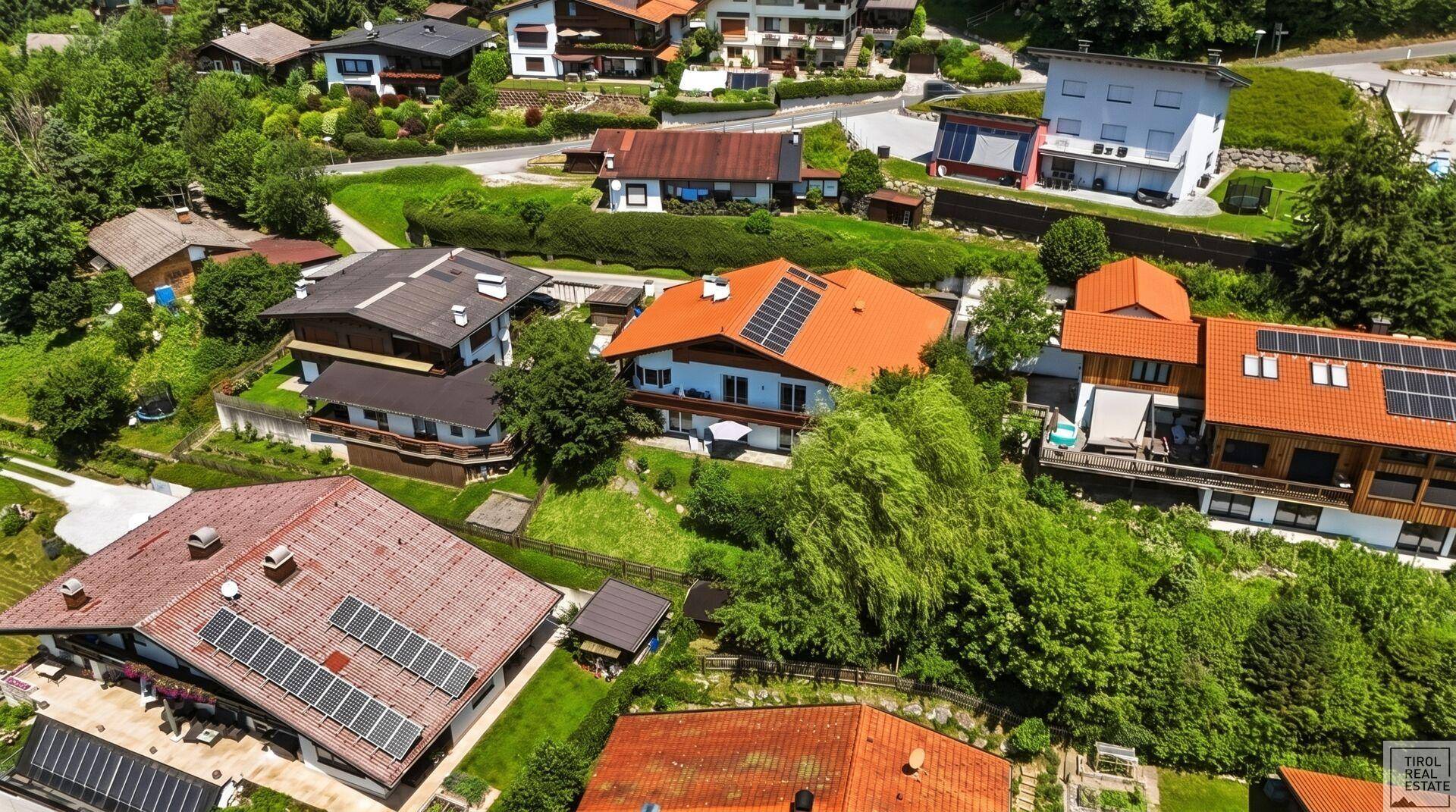 Vogelperspektive einer Wohnsiedlung mit Häusern, grünen Gärten und einigen Dächern mit Solaranlagen.