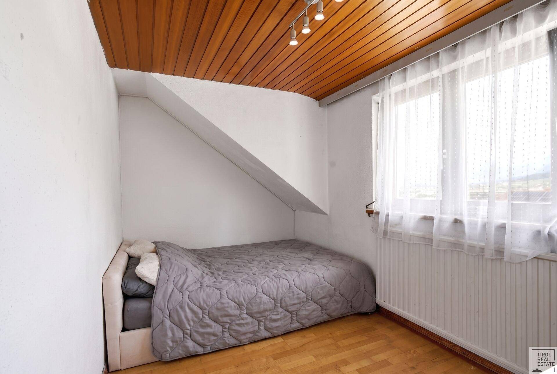 Schlafzimmer mit Dachschräge, Holzboden und Fenster für natürliches Licht.