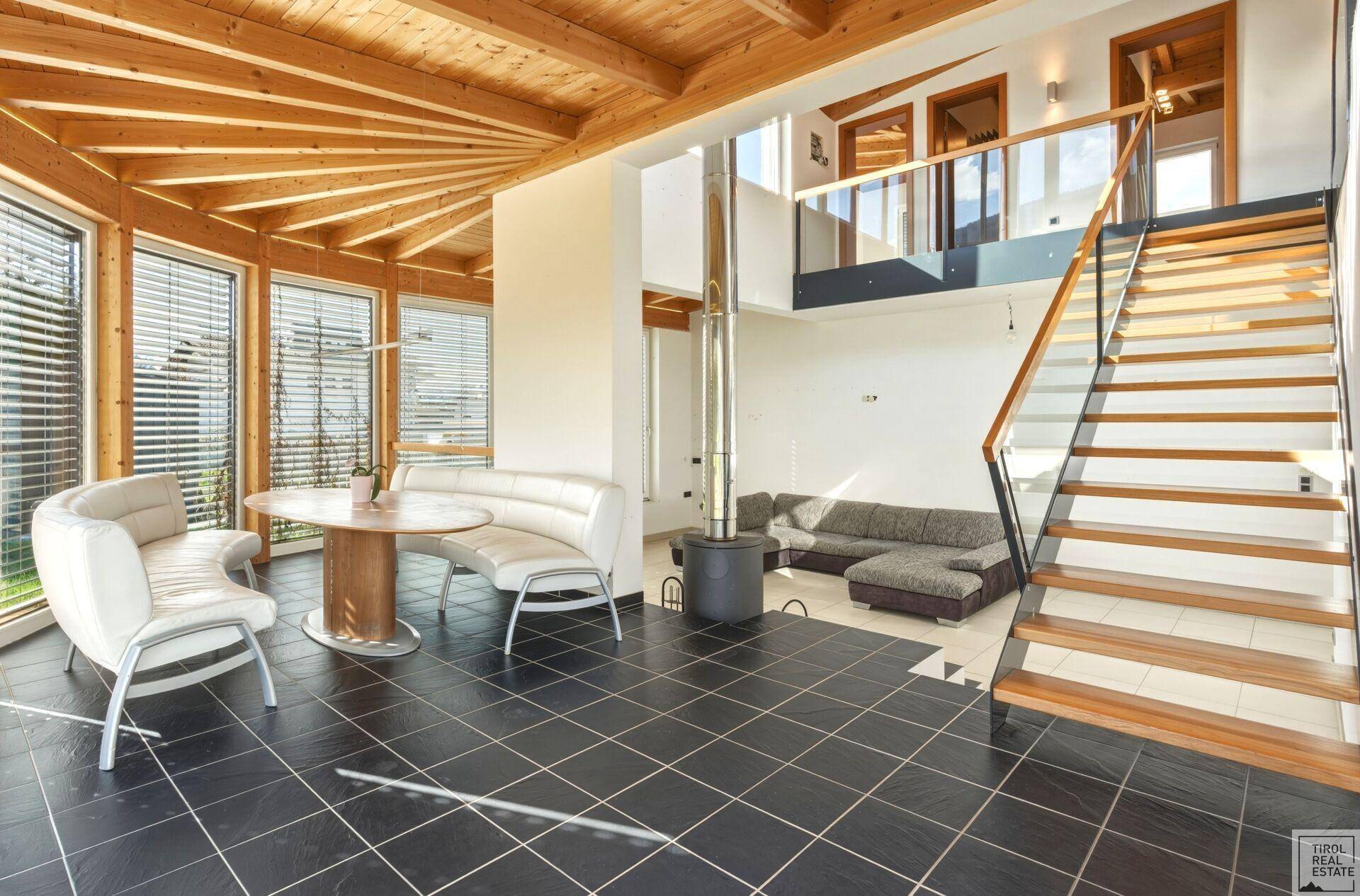 Offener Wohnbereich mit hoher Decke, Holzbalken und moderner Treppe, verbunden mit einem Essbereich.