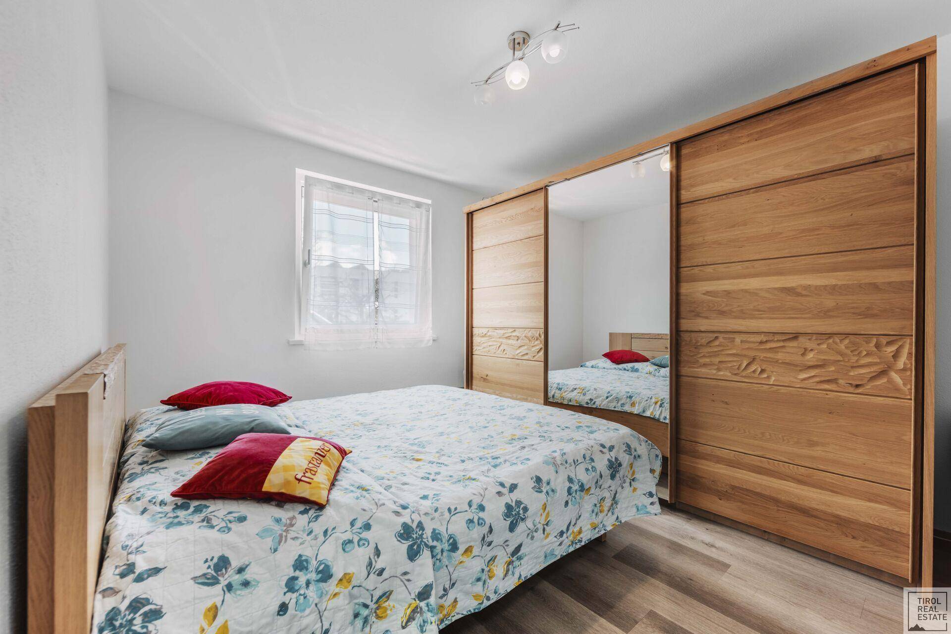 Gemütliches Schlafzimmer mit Holzbett, Spiegelschrank und Fenster mit Blick nach draußen.