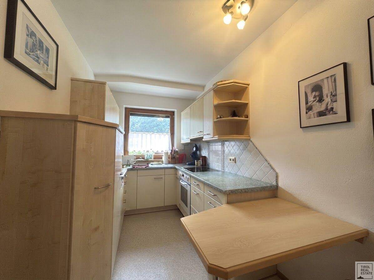 Funktionale Küche mit hellen Holzschränken, Fenster und ausklappbarem Esstisch.