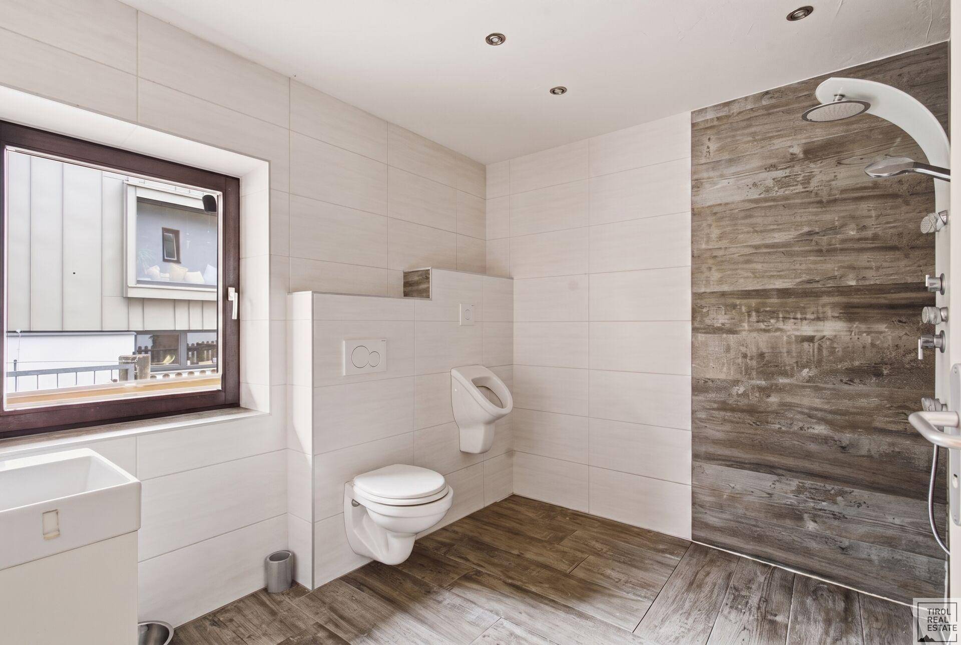 Modernes Badezimmer mit begehbarer Dusche, Wand-WC, Urinal und Fenster für Tageslicht.