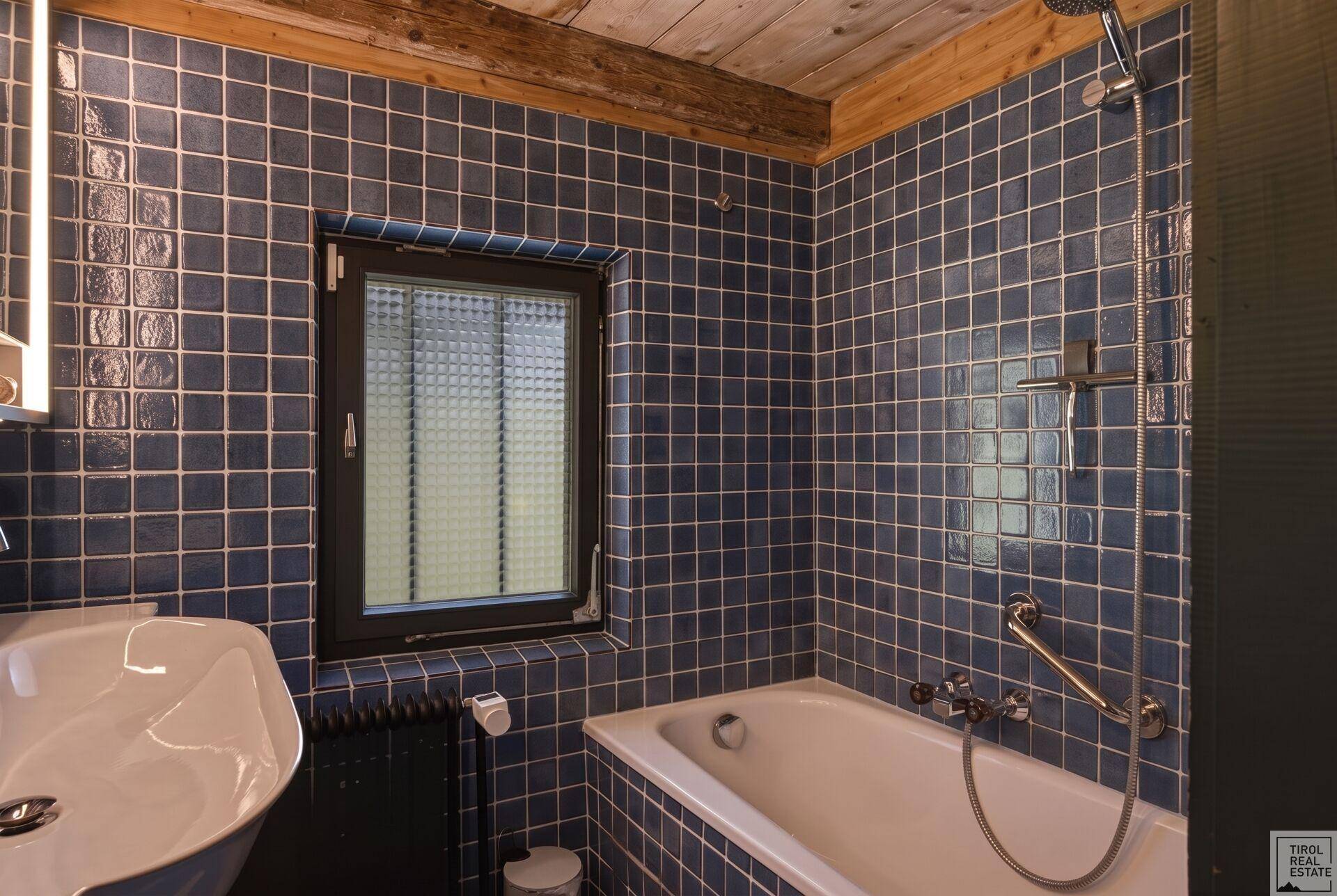 Badezimmer mit blauen Fliesen, Badewanne und Fenster für Tageslicht.