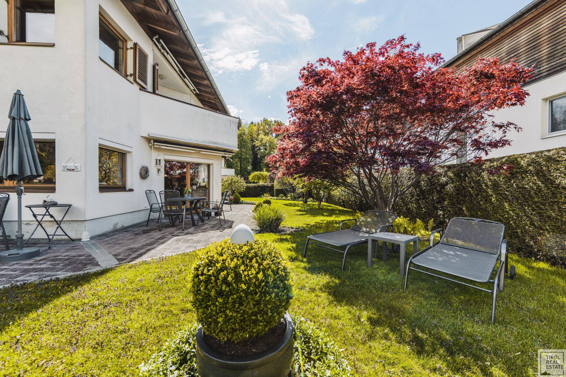Weitläufiger Garten mit Rasen, Liegestühlen und einer Terrasse mit Essbereich am Haus.