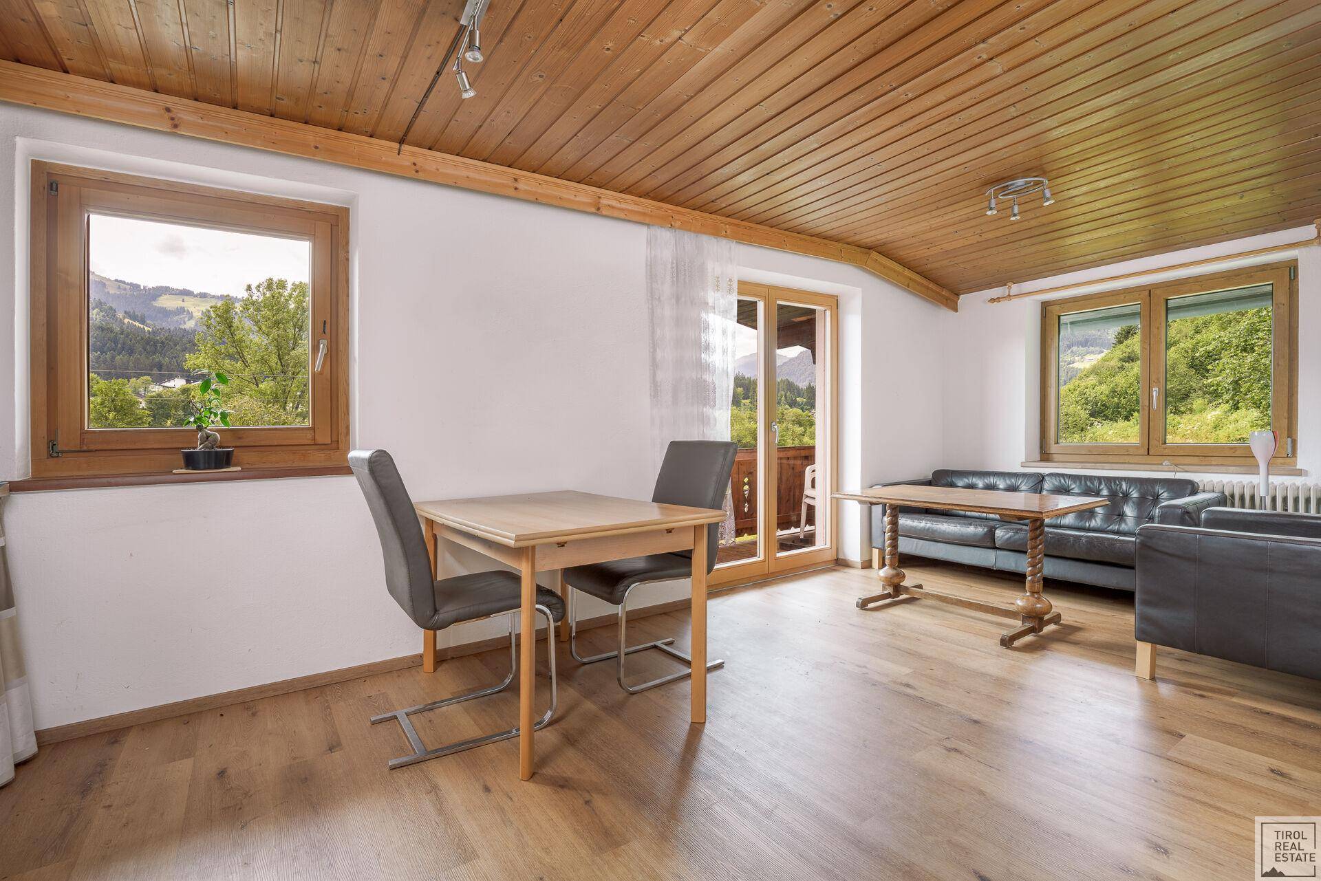 Heller Wohnraum mit Holzboden, Holzbalkendecke und Bergblick vom angrenzenden Balkon.