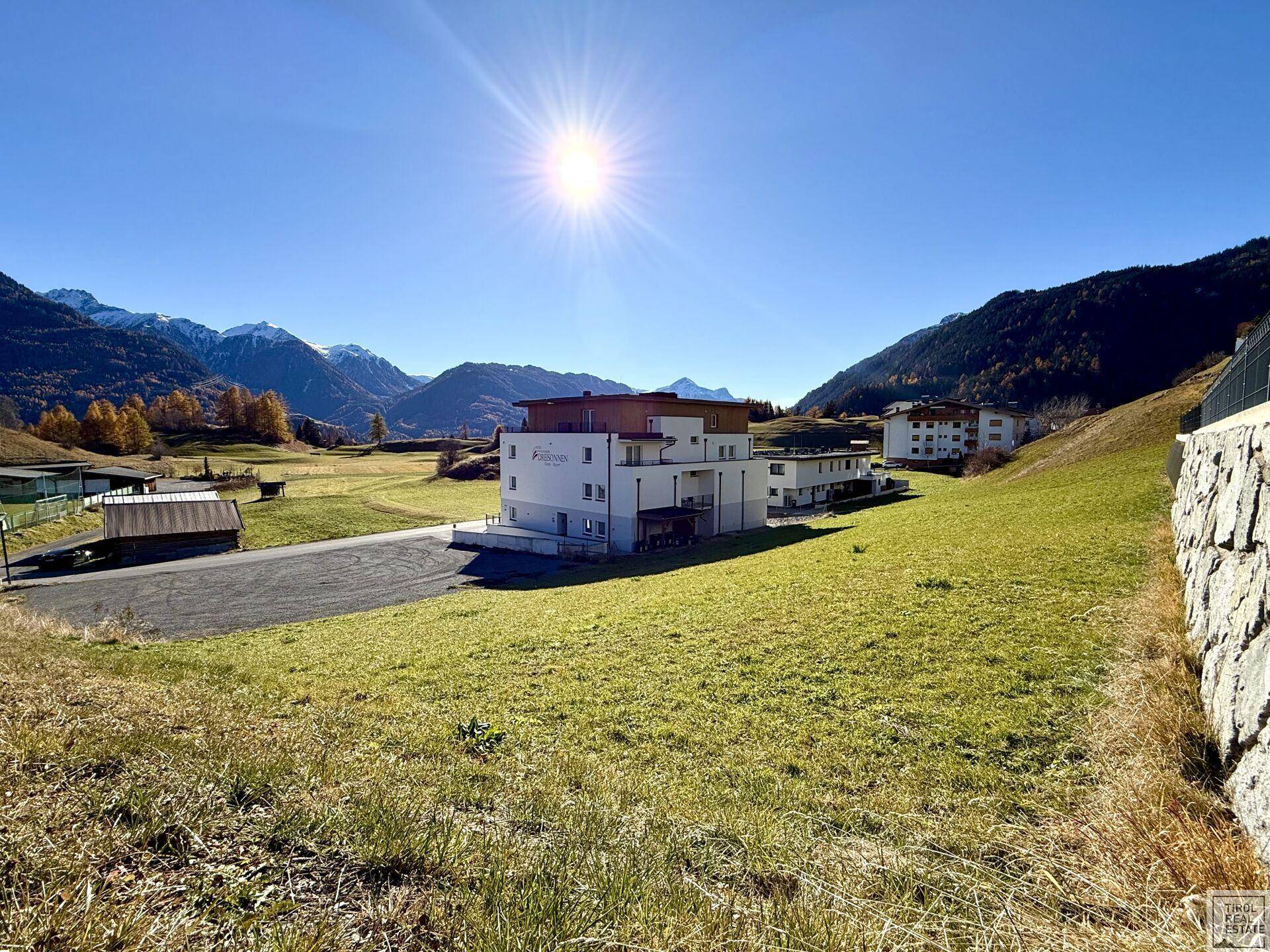 Sonnige Außenansicht eines modernen Gebäudes inmitten einer grünen Landschaft mit Alpenpanorama.