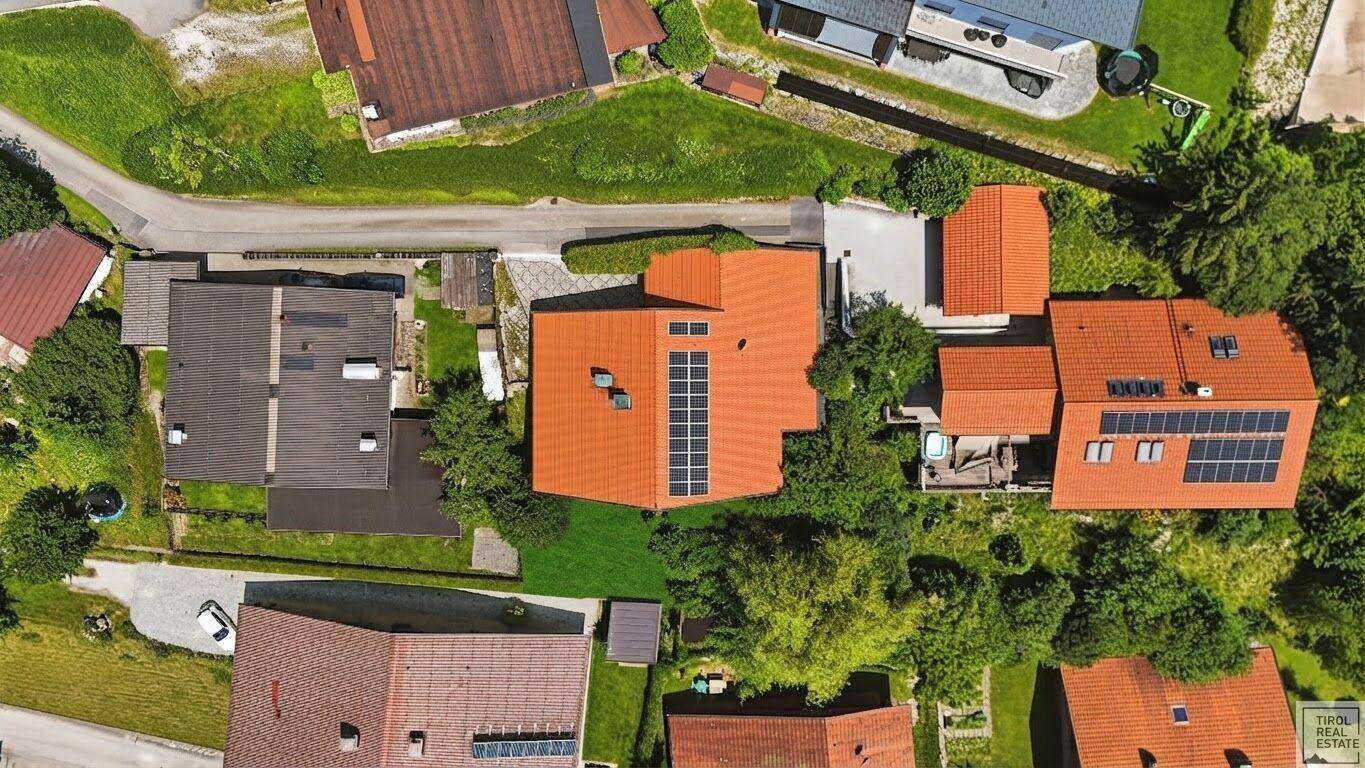 Draufsicht auf eine Wohnsiedlung mit Häusern, grünen Gärten und Dächern, die mit Solaranlagen ausgestattet sind.