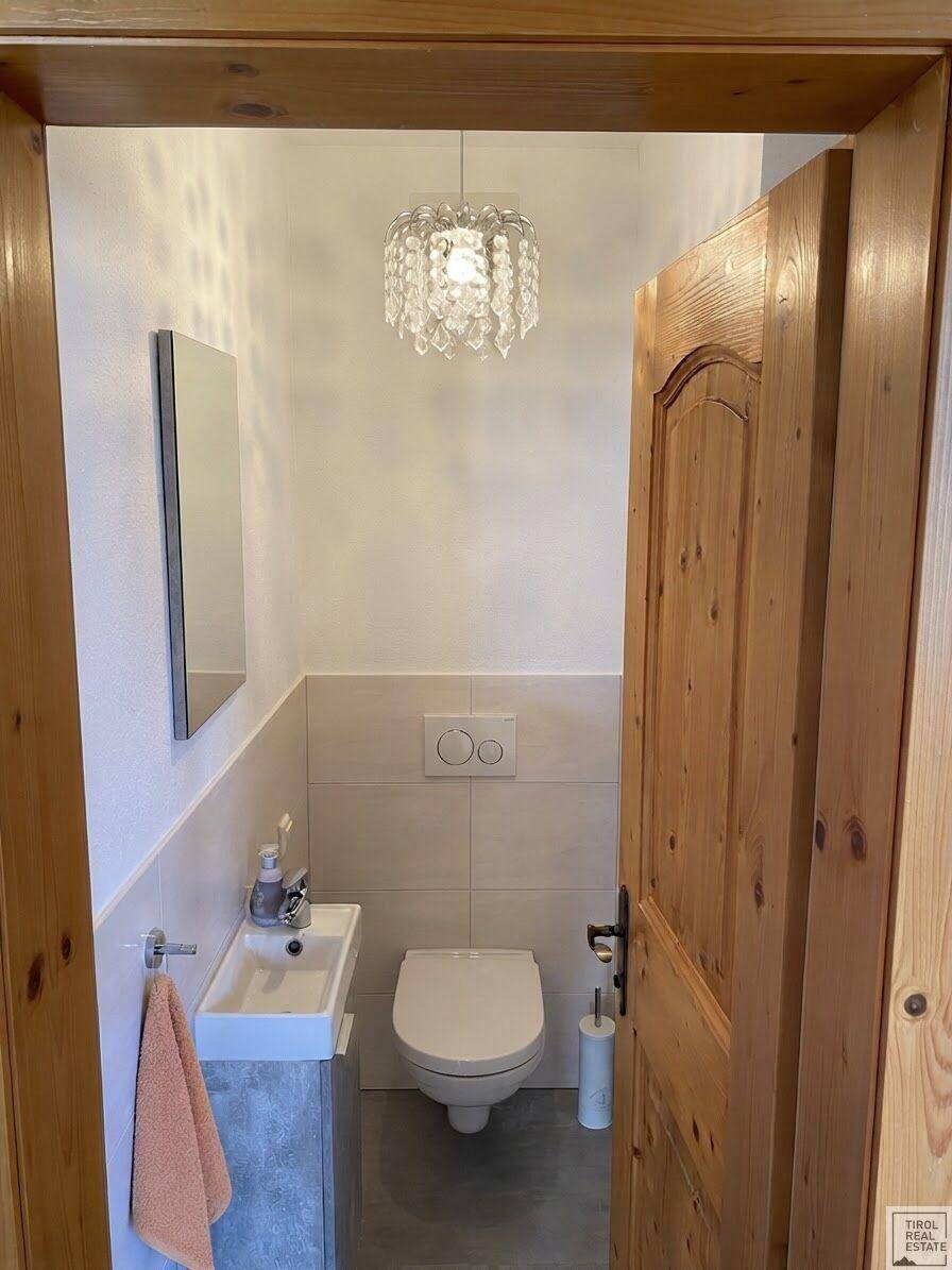 Kleines Gäste-WC mit modernem Waschtisch, wandhängender Toilette und einem dekorativen Kronleuchter.
