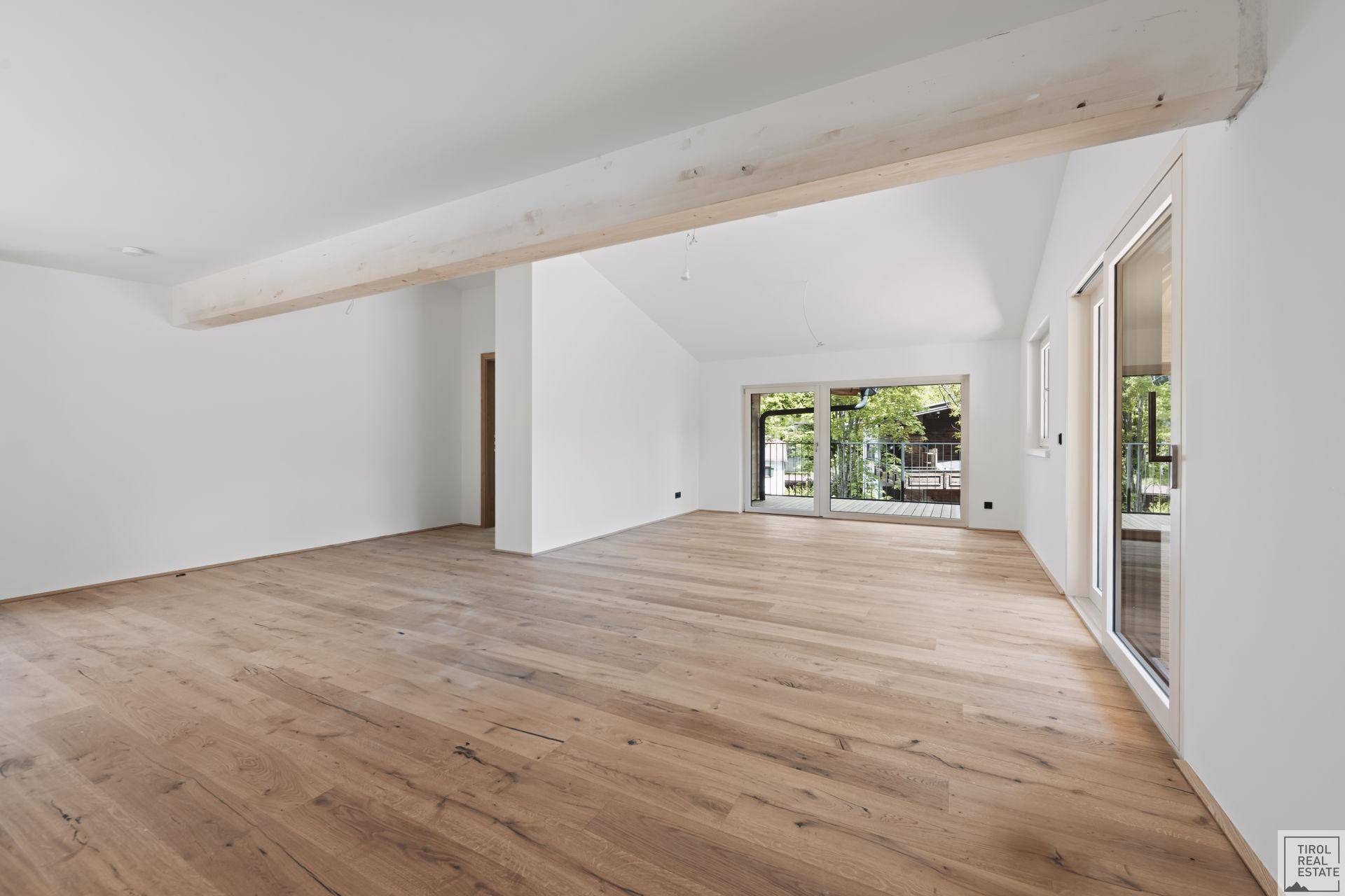 Lichtdurchfluteter Wohnraum mit Holzbalken, Eichenparkett und Zugang zu einem Außenbereich.