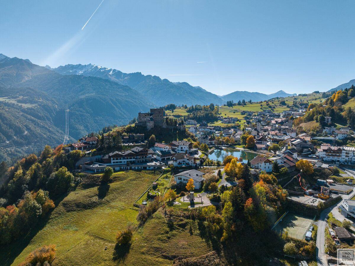 Weitläufige Luftaufnahme eines charmanten Bergdorfes mit See und umliegender Naturlandschaft.