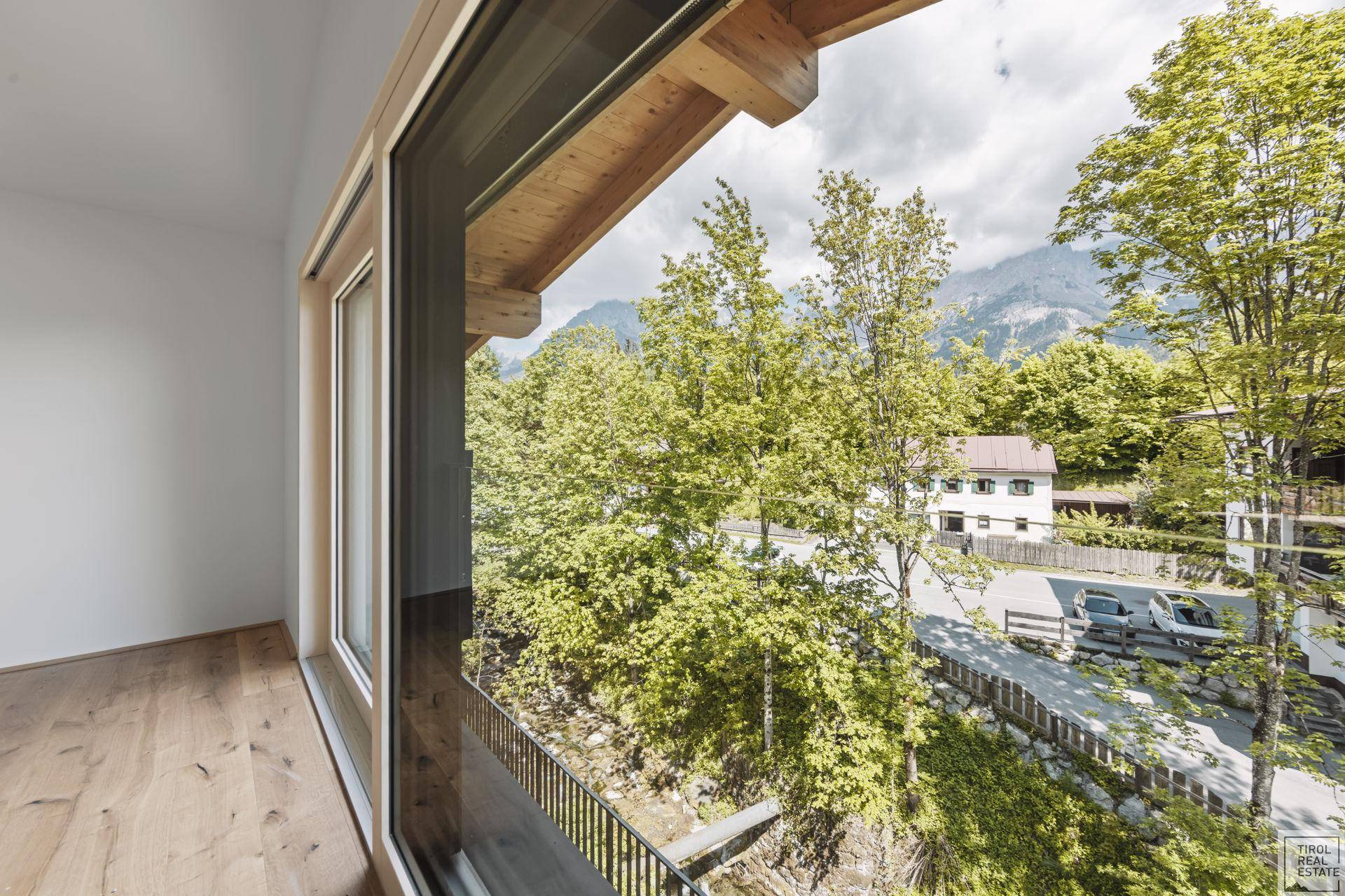 Ausblick aus einem großen Fenster auf grüne Bäume und die umliegende Berglandschaft.