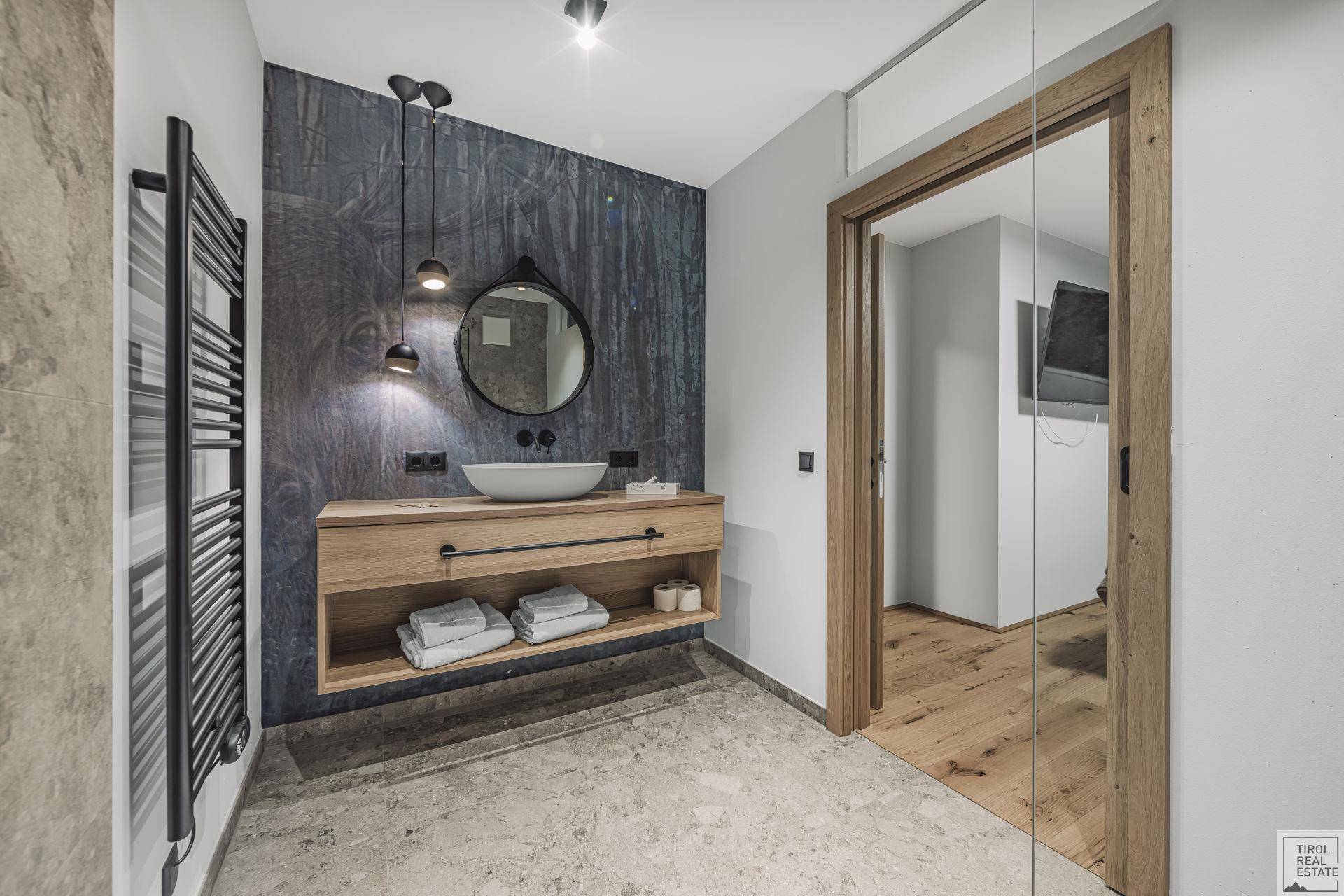Modernes Badezimmer mit schwebendem Waschtisch, rundem Spiegel und beheiztem Handtuchhalter.
