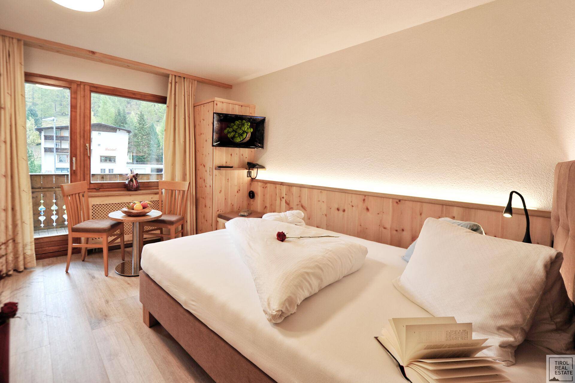 Schlafzimmer mit Einzelbett, Balkonzugang und Blick auf die bewaldete Berglandschaft.
