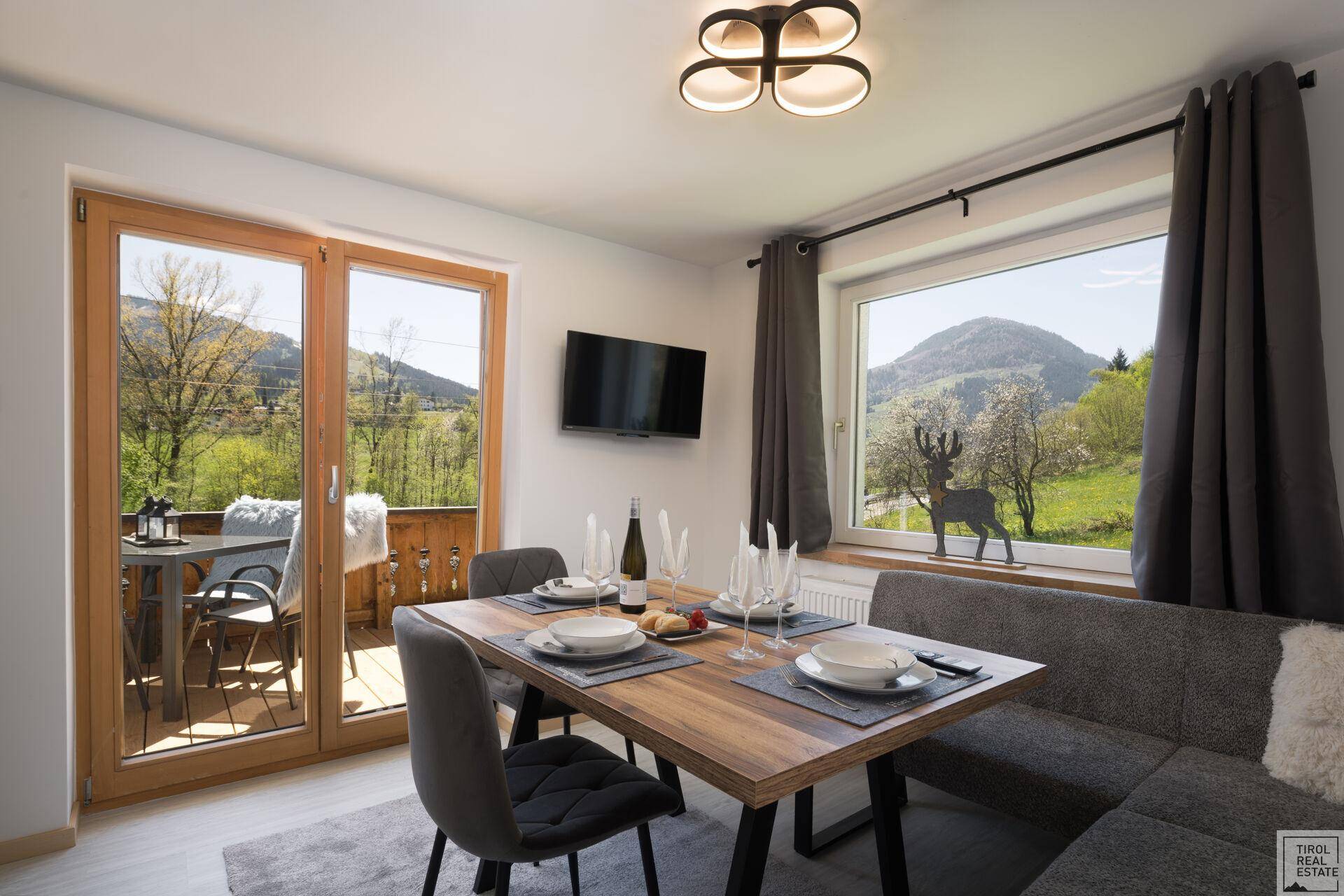 Moderner Essbereich mit Holztisch, Sitzbank und Zugang zum Balkon mit Bergblick.