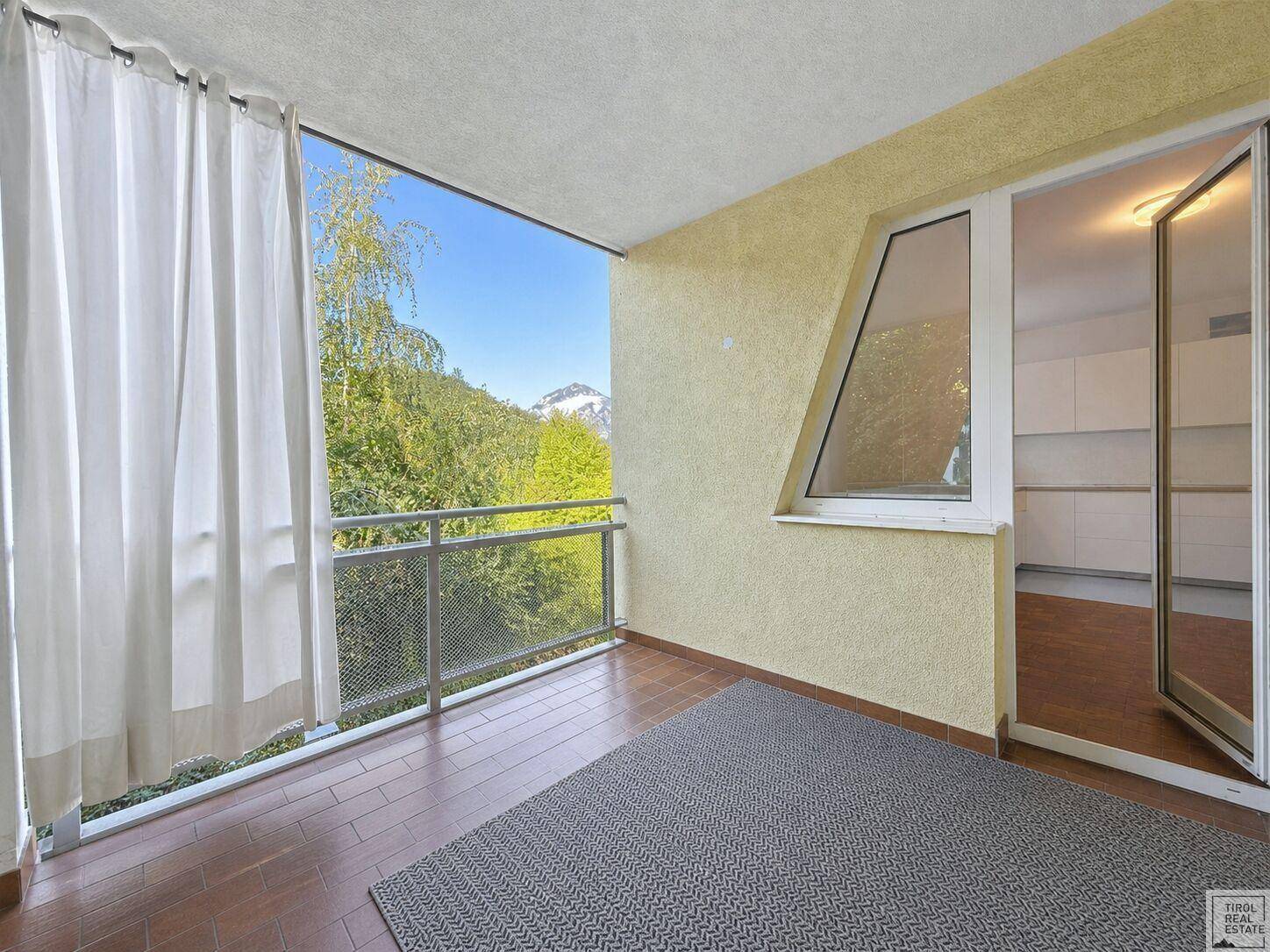 Heller Balkon mit Teppich und Vorhängen, der einen schönen Blick auf die Berge und Bäume bietet.