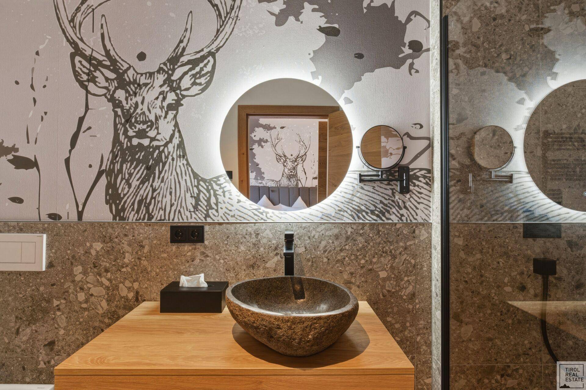 Modernes Badezimmer mit Steinwaschbecken, beleuchtetem Spiegel und Hirschmotiv-Wand.