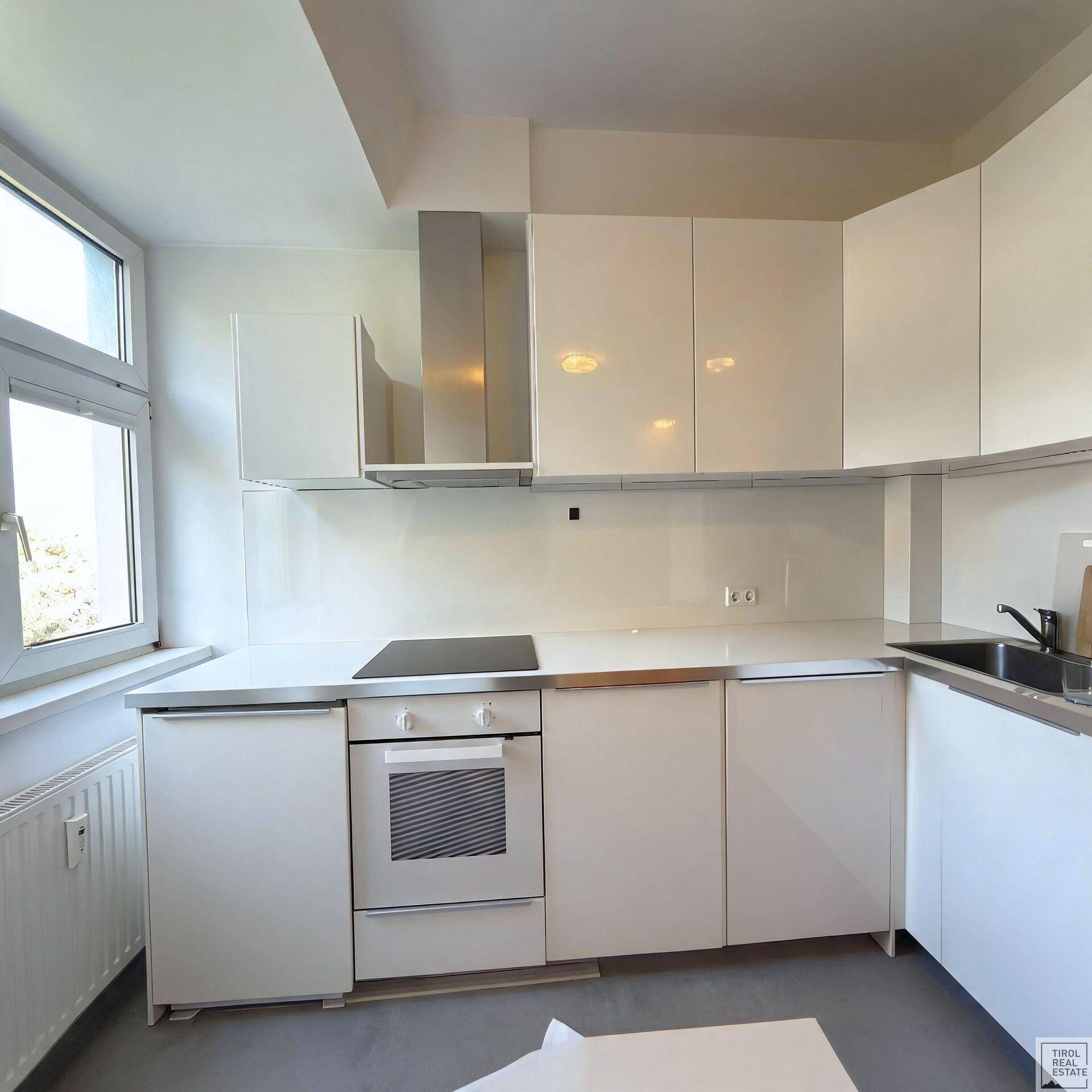 Moderne, weiße Einbauküche mit Induktionskochfeld, Backofen und Dunstabzugshaube, hell und funktional.